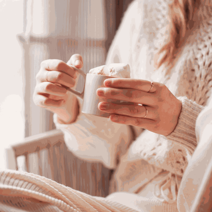 A girl holding a cup of hot chocolate in her beige cozy outfit