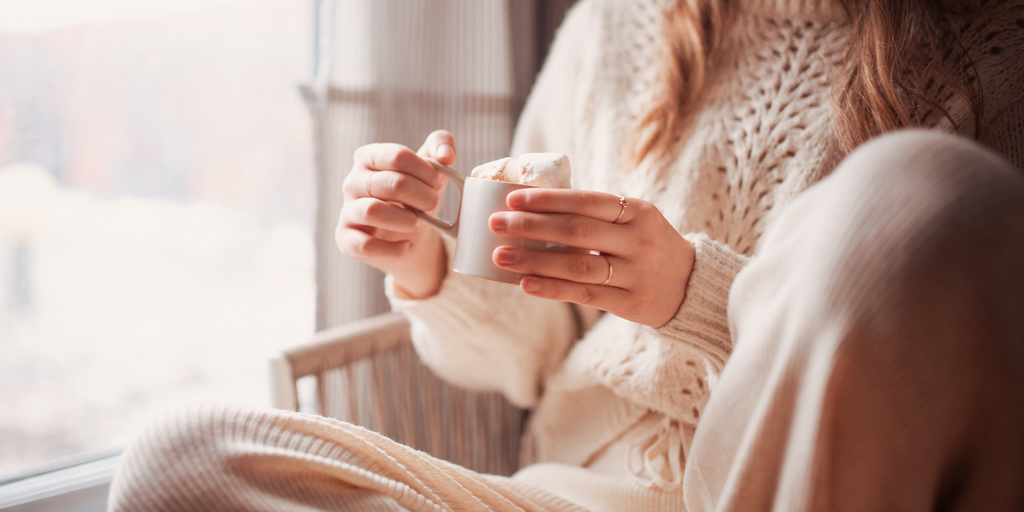 A girl holding a cup of hot chocolate in her beige cozy outfit