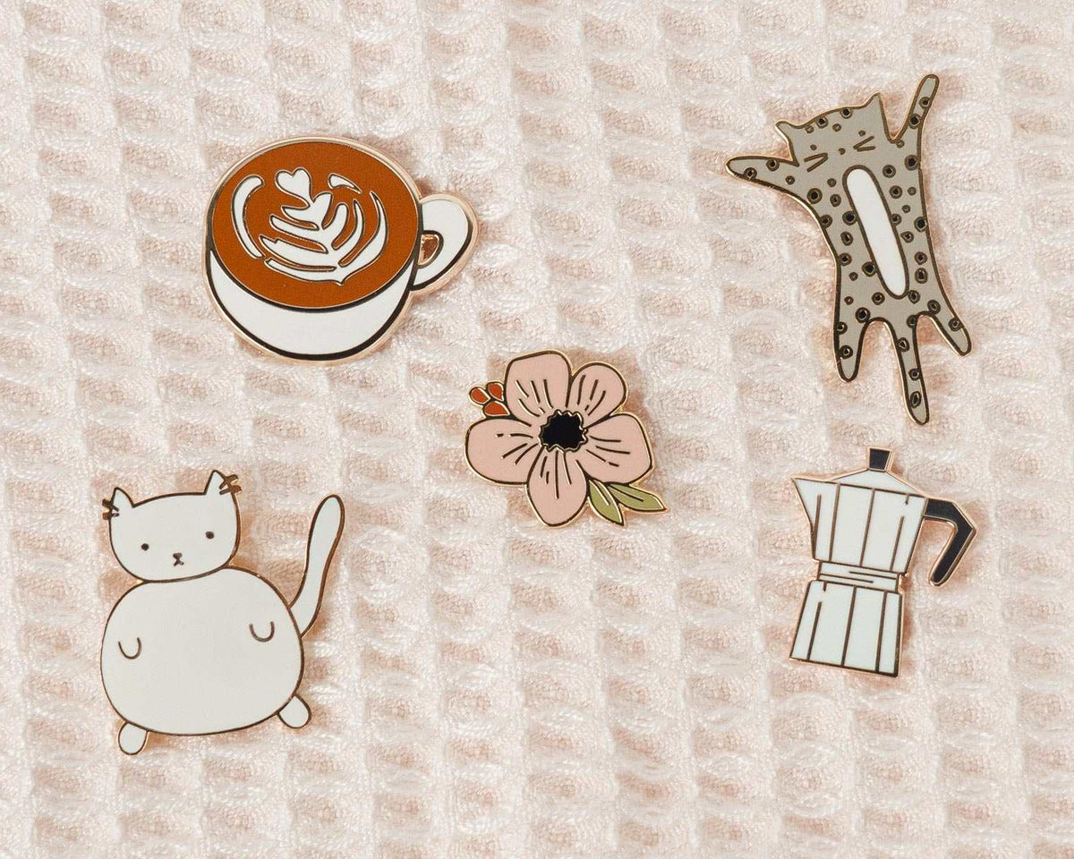 Collection of illustrated enamel pins featuring playful and cozy designs by Mimi & August