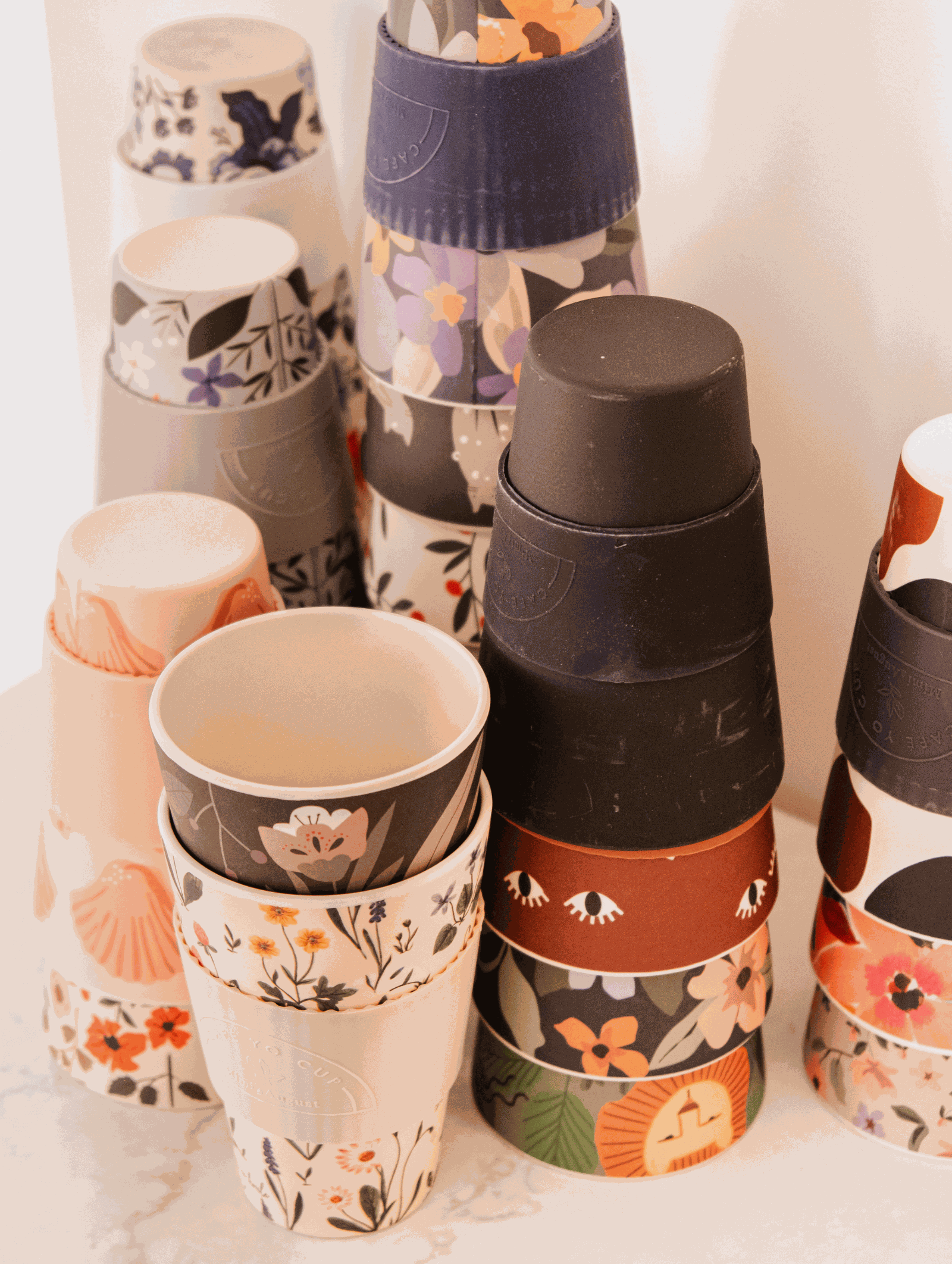 A group of Defect Café Yo Cups with different designs on them, including a silicone lid by Mimi & August.