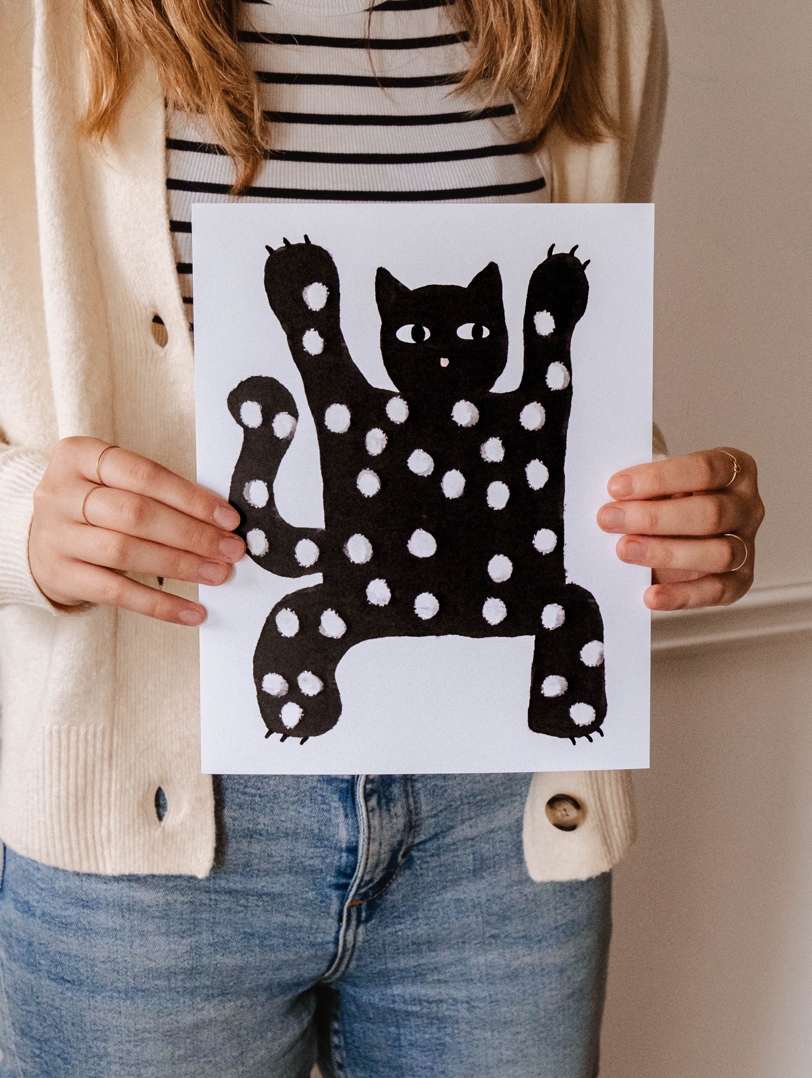 A cat lover proudly holds up a Mimi & August Scary Black Cat Art Print.