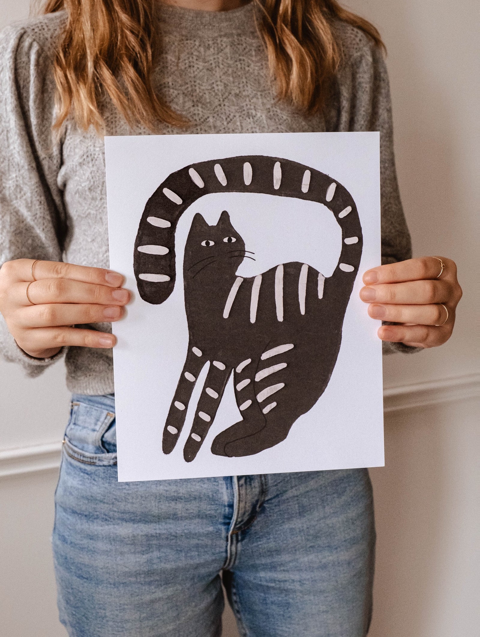 A woman peacefully holding up a Mimi & August Calm Black Cat Art Print.