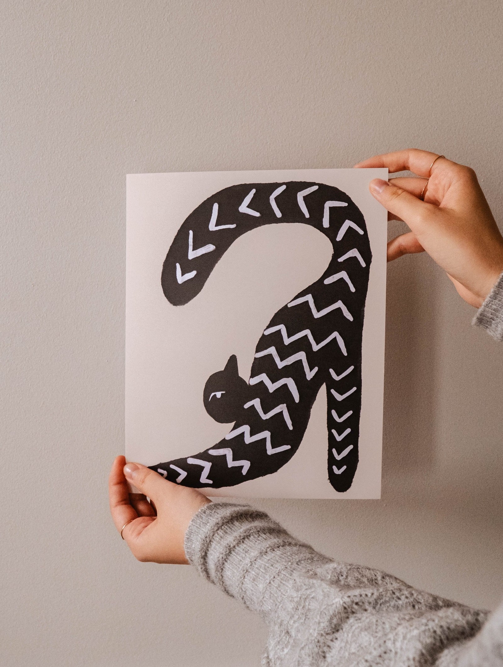 A woman proudly displaying a "Stretchy Black Cat Art Print" by Mimi & August.