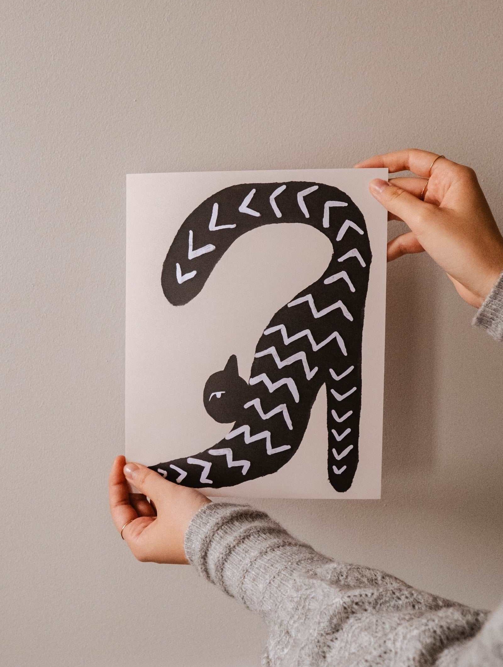 A woman proudly displaying a "Stretchy Black Cat Art Print" by Mimi & August.