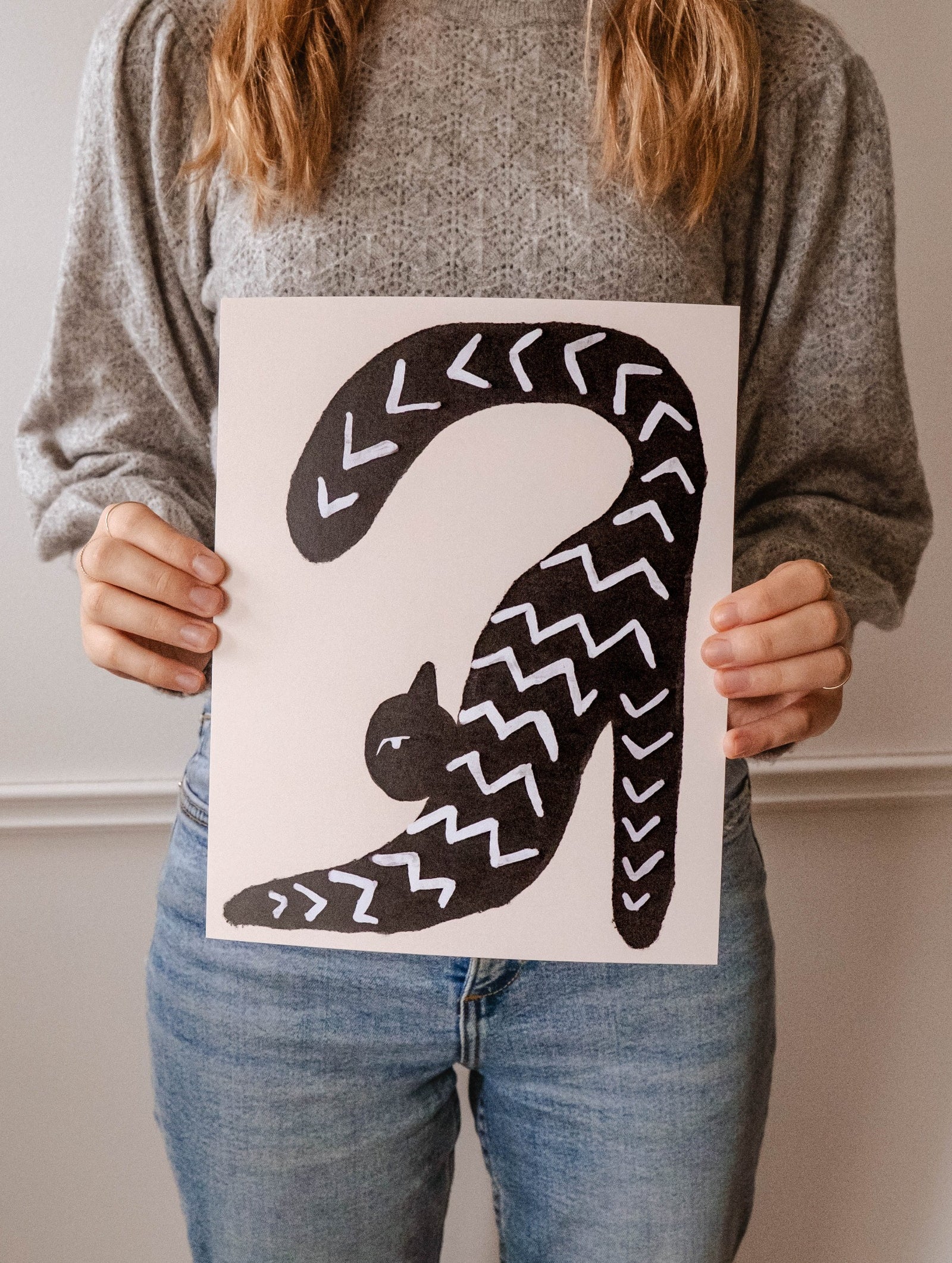 A woman holding up a Stretchy Black Cat Art Print by Mimi & August in a yoga-like posture.