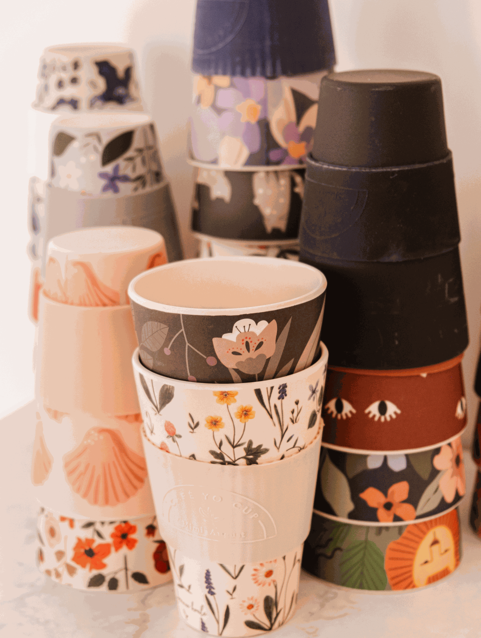 A stack of Mimi & August Defect Café Yo Cups with different designs on them, including recyclable options.