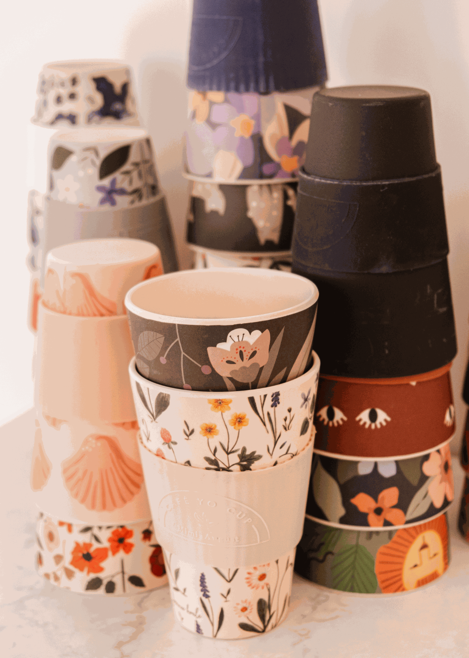 A stack of Mimi & August Defect Café Yo Cups with different designs on them, including recyclable options.