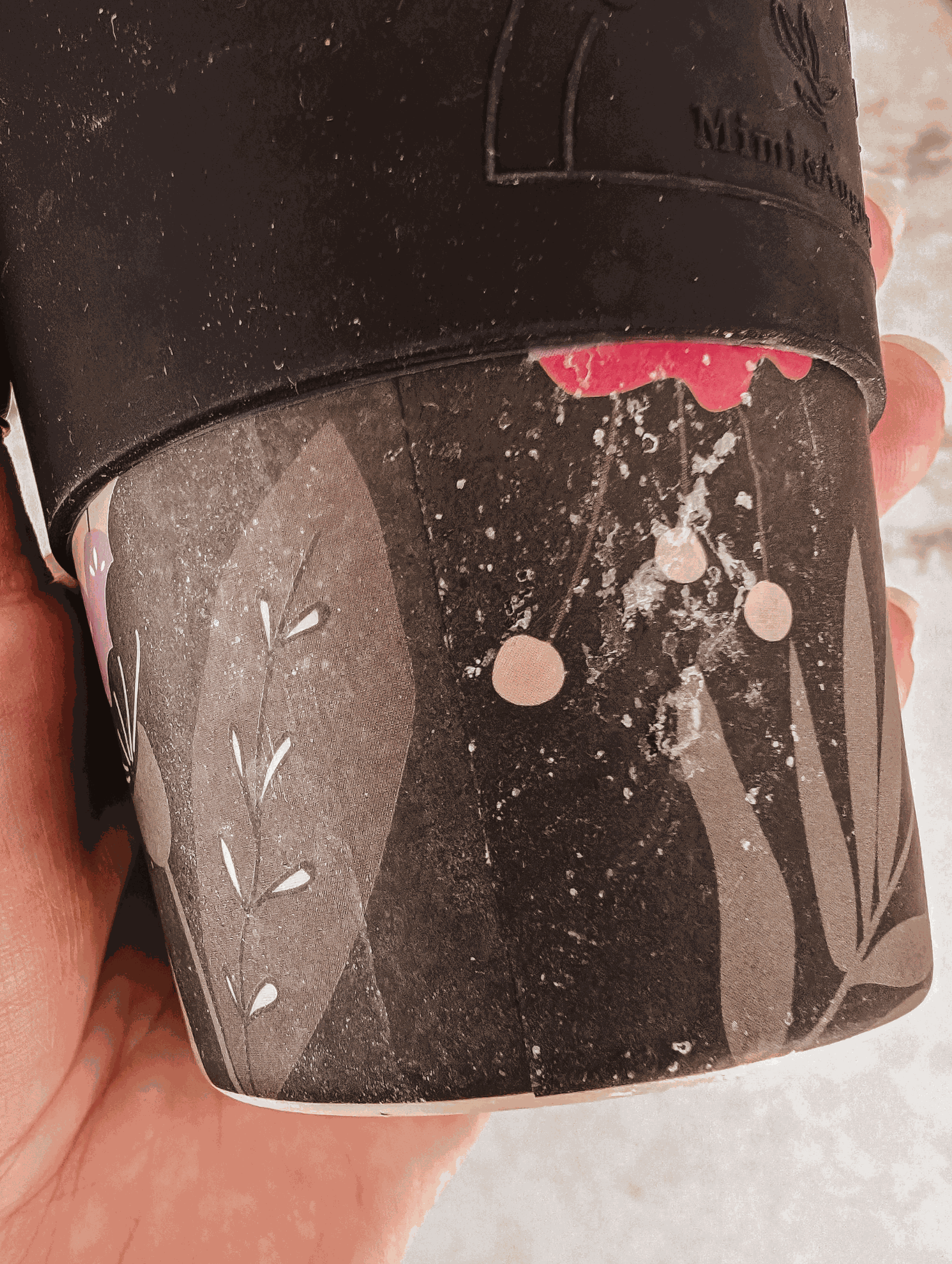 A person holding a Mimi & August Defect Café Yo Cup with flowers on it.