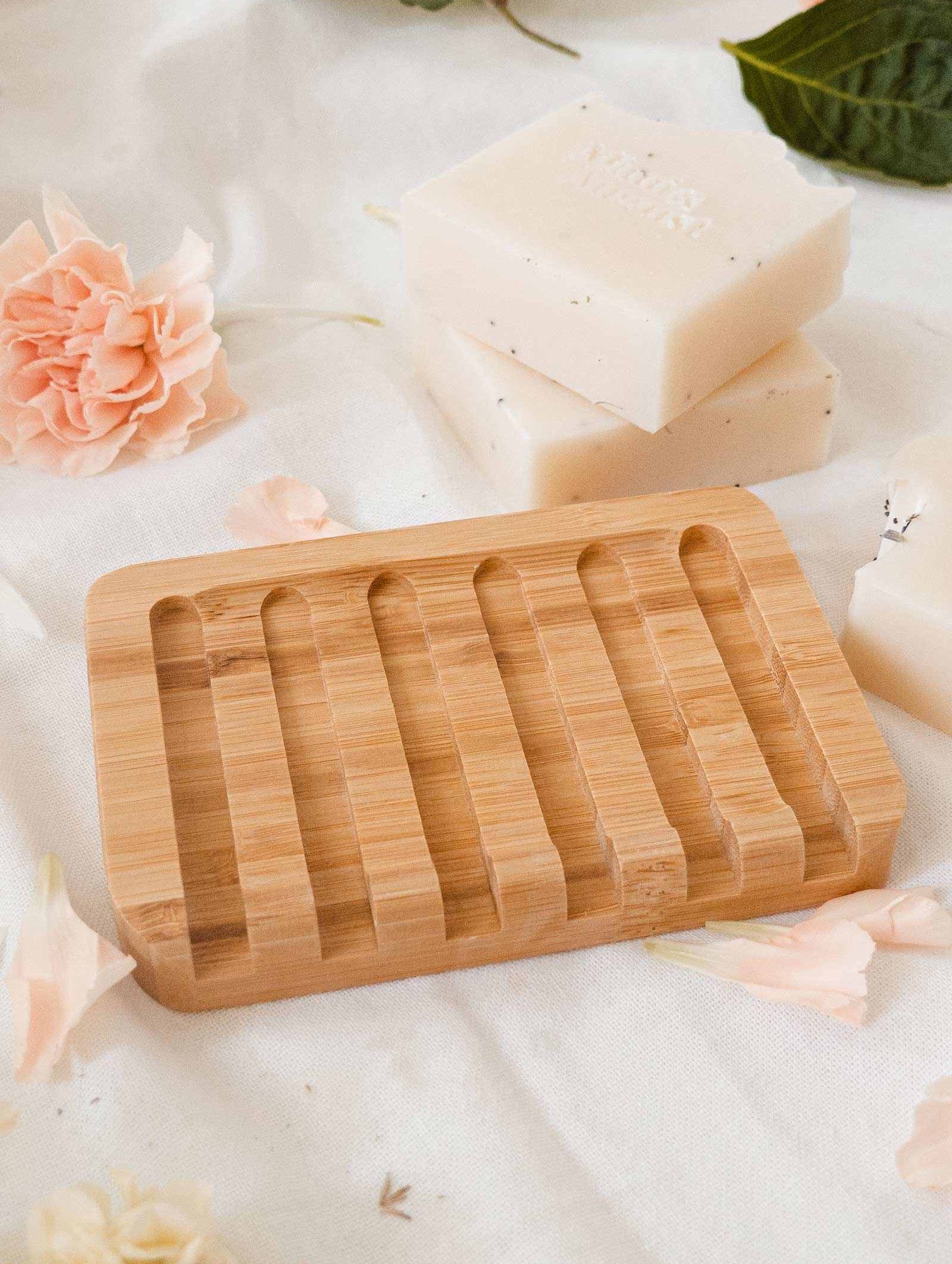 A durable mimi and august Bamboo soap dish with soaps and flowers on a table.