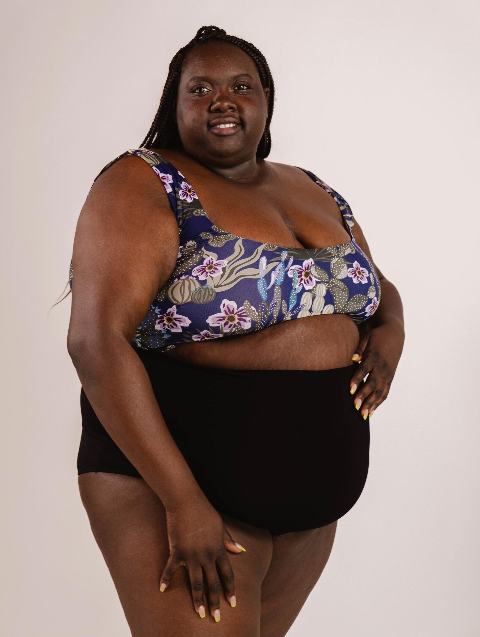 A person wearing a floral patterned swimming top and Mimi & August's Bermudes Black extra high waisted bikini bottom, standing against a plain background, creating a flattering silhouette.