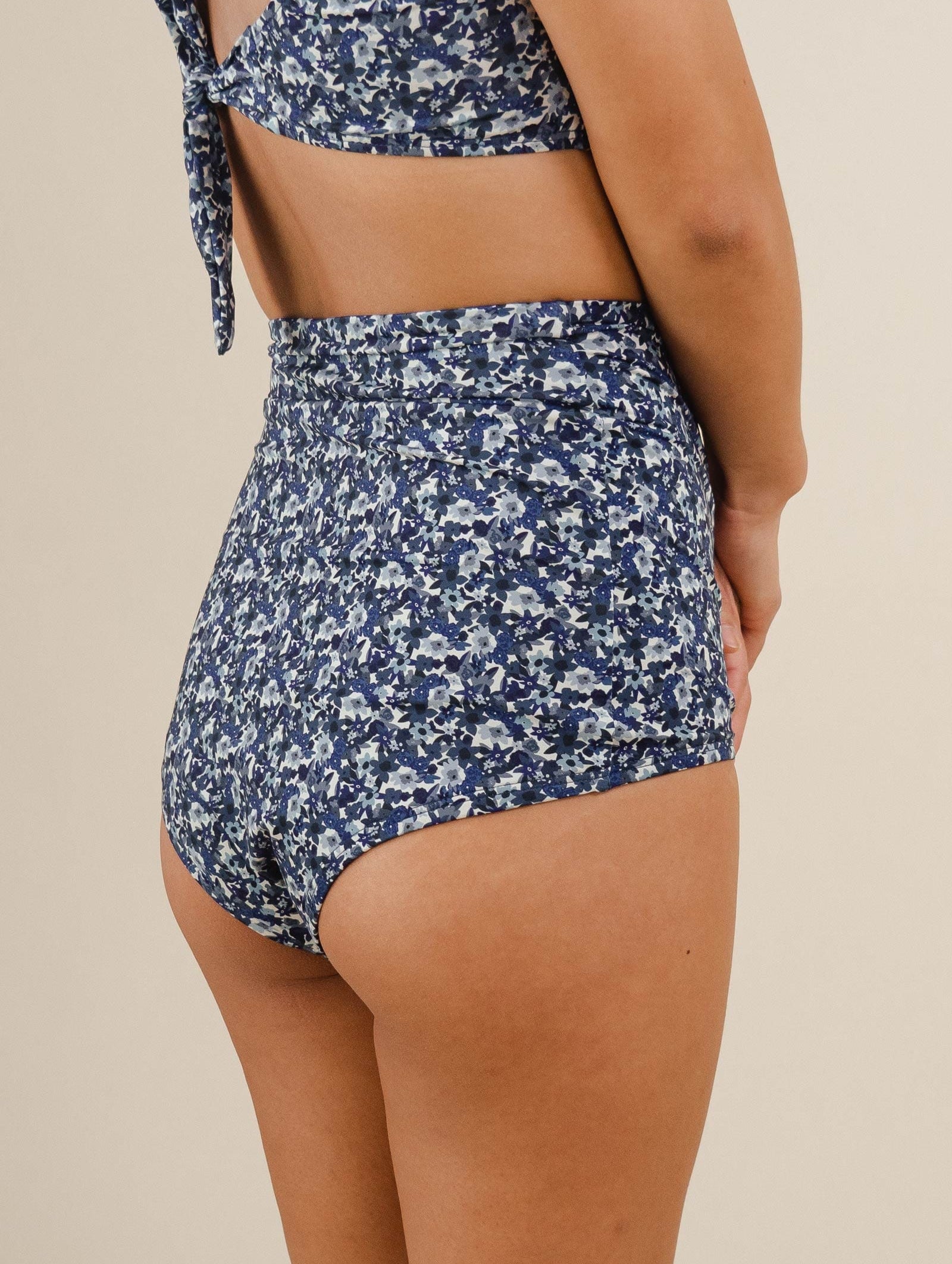 The back of a woman in Mimi and August's comfiest swimsuit with their blue floral High Waist Bikini Bottom.