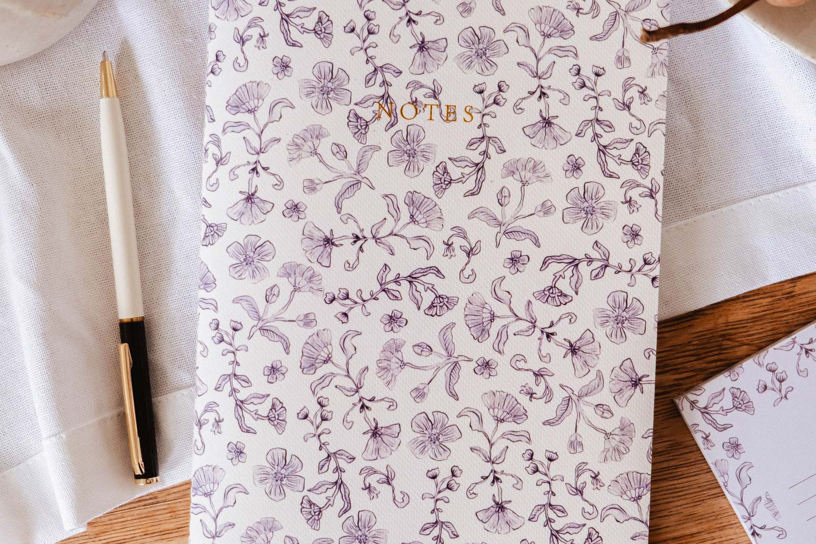 The Blossom - Notebook by Mimi & August, labeled "NOTES," rests on a wooden surface beside a pen, pears, and a white cloth—ideal as a lined journal for capturing your thoughts.