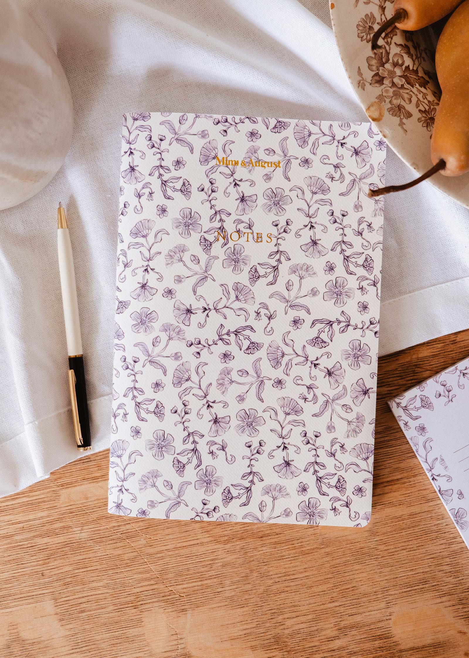 The Blossom - Notebook by Mimi & August, labeled "NOTES," rests on a wooden surface beside a pen, pears, and a white cloth—ideal as a lined journal for capturing your thoughts.