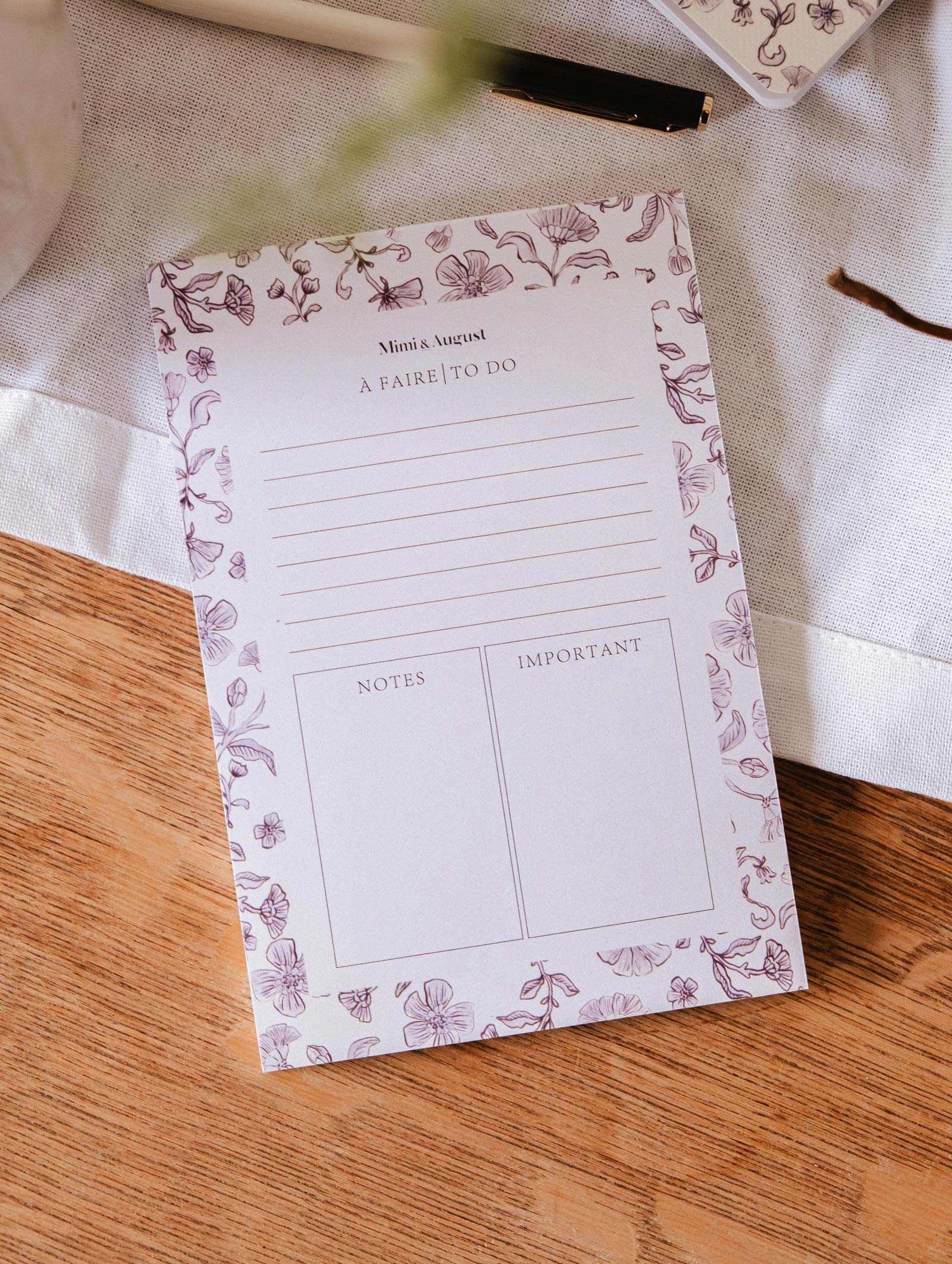 The Blossom - Notepad by Mimi & August, crafted from recycled paper with sections for tasks, notes, and important items, rests on a wooden table beside a pen and a white cloth.