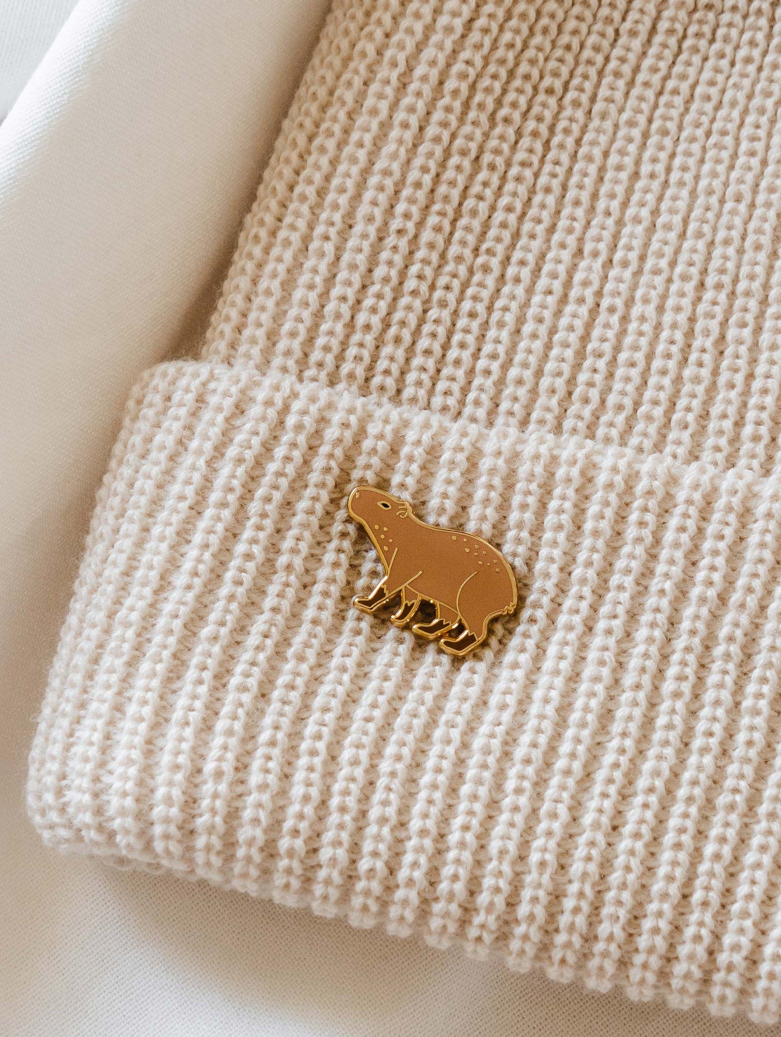A Capybara enamel pin in a cream beanie by mimi and august