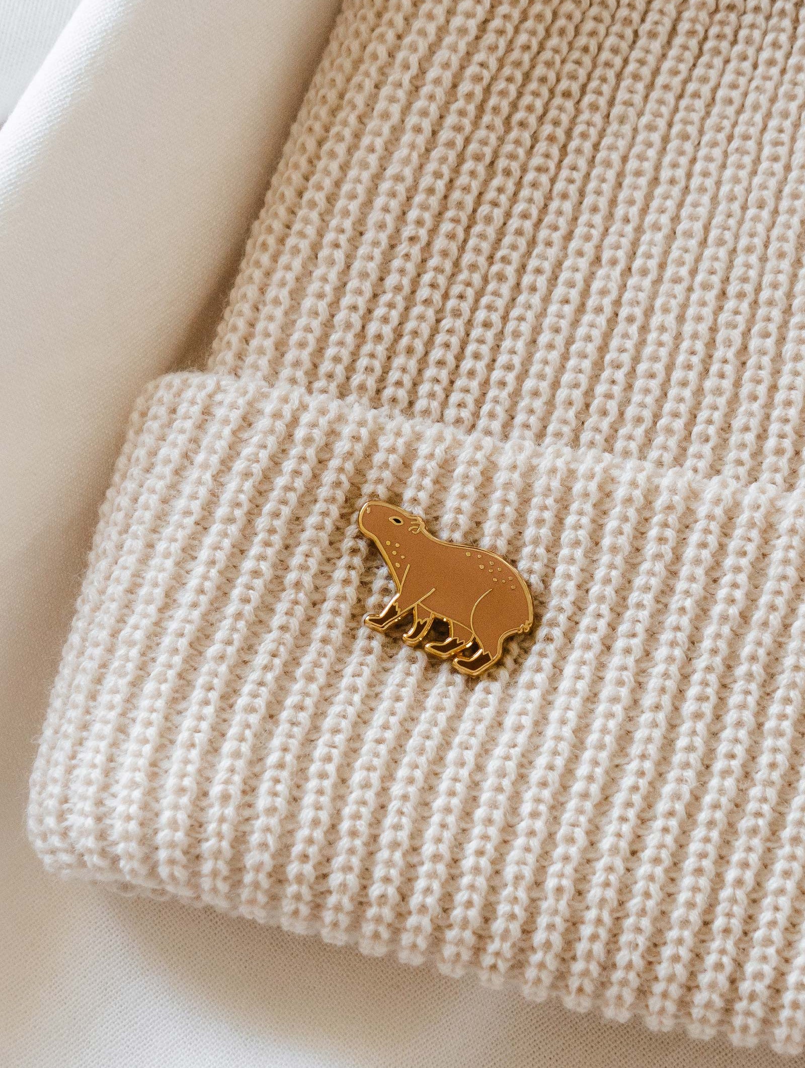 A Capybara enamel pin in a cream beanie by mimi and august