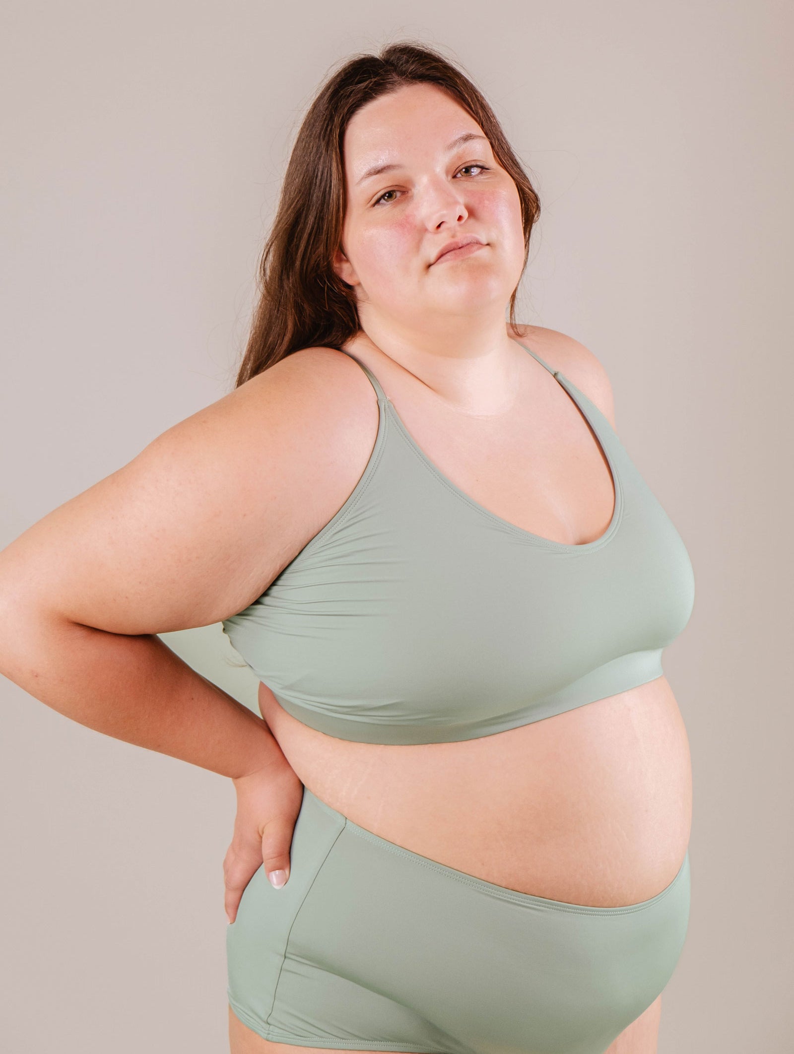 Woman wearing a green Chichi Agave Bralette Bikini Top from Mimi & August and matching leggings, standing with one hand on hip, neutral background.