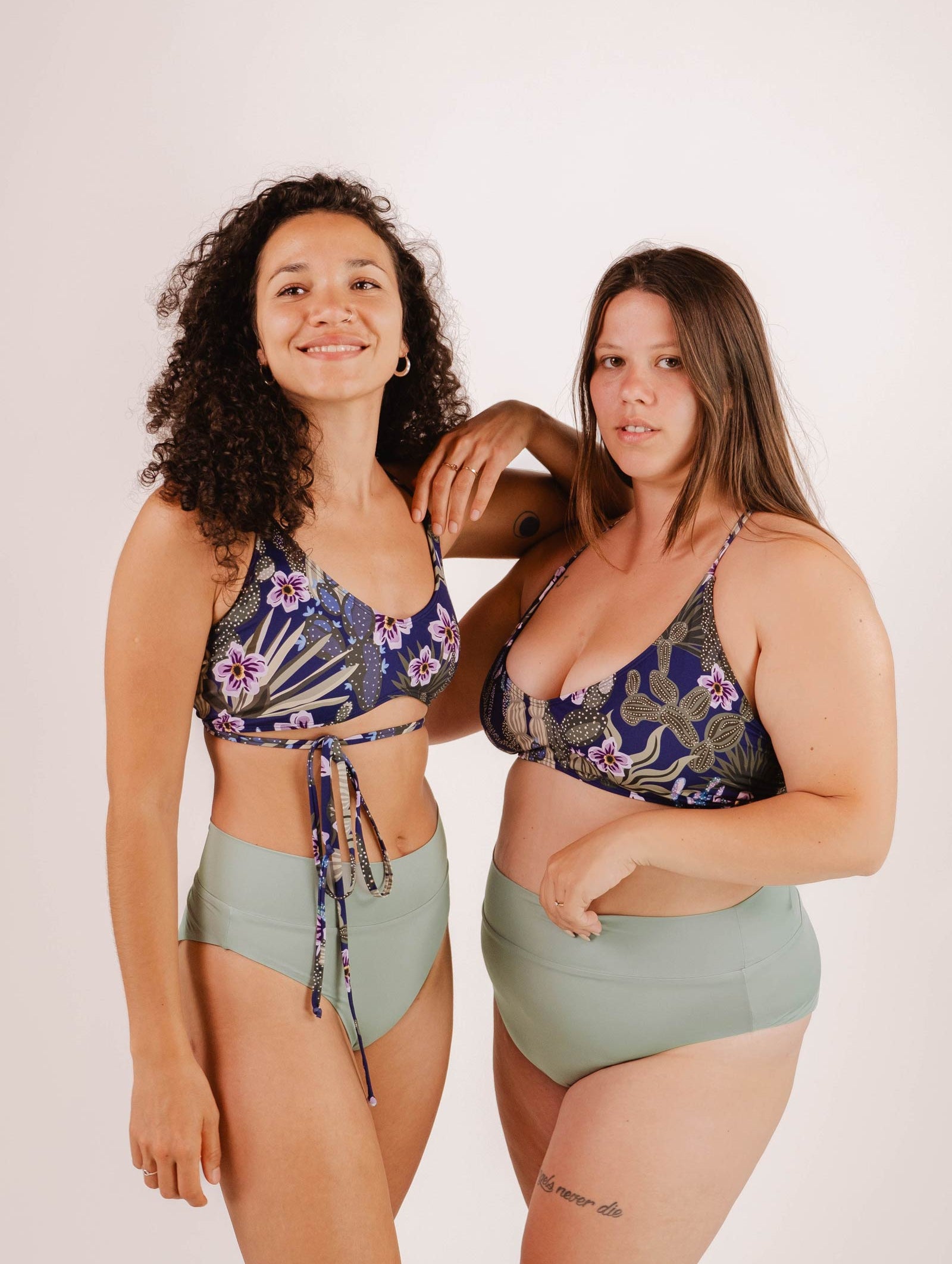 Two women pose together in Chichi Jardin de Nuit - Bralette Bikini Tops by Mimi & August with green high-waisted bottoms against a plain background, looking at the camera.
