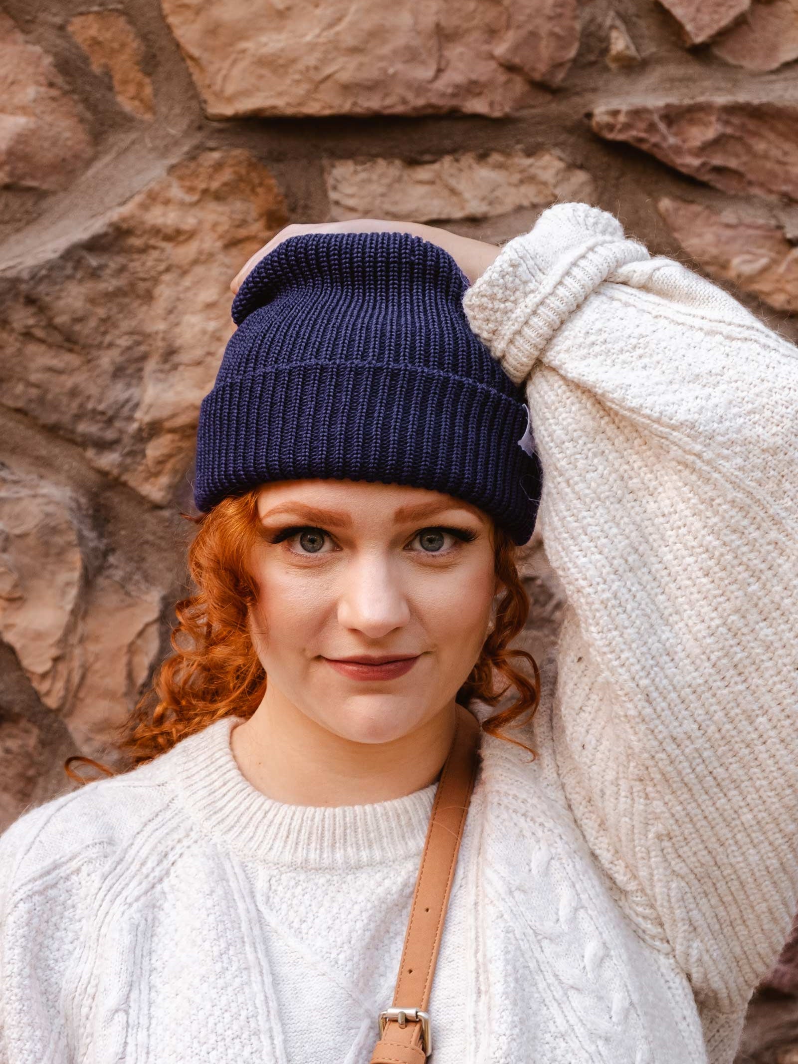 A woman wearing a Deep Blue Cuffed Beanie by mimi and august against a stone wall.