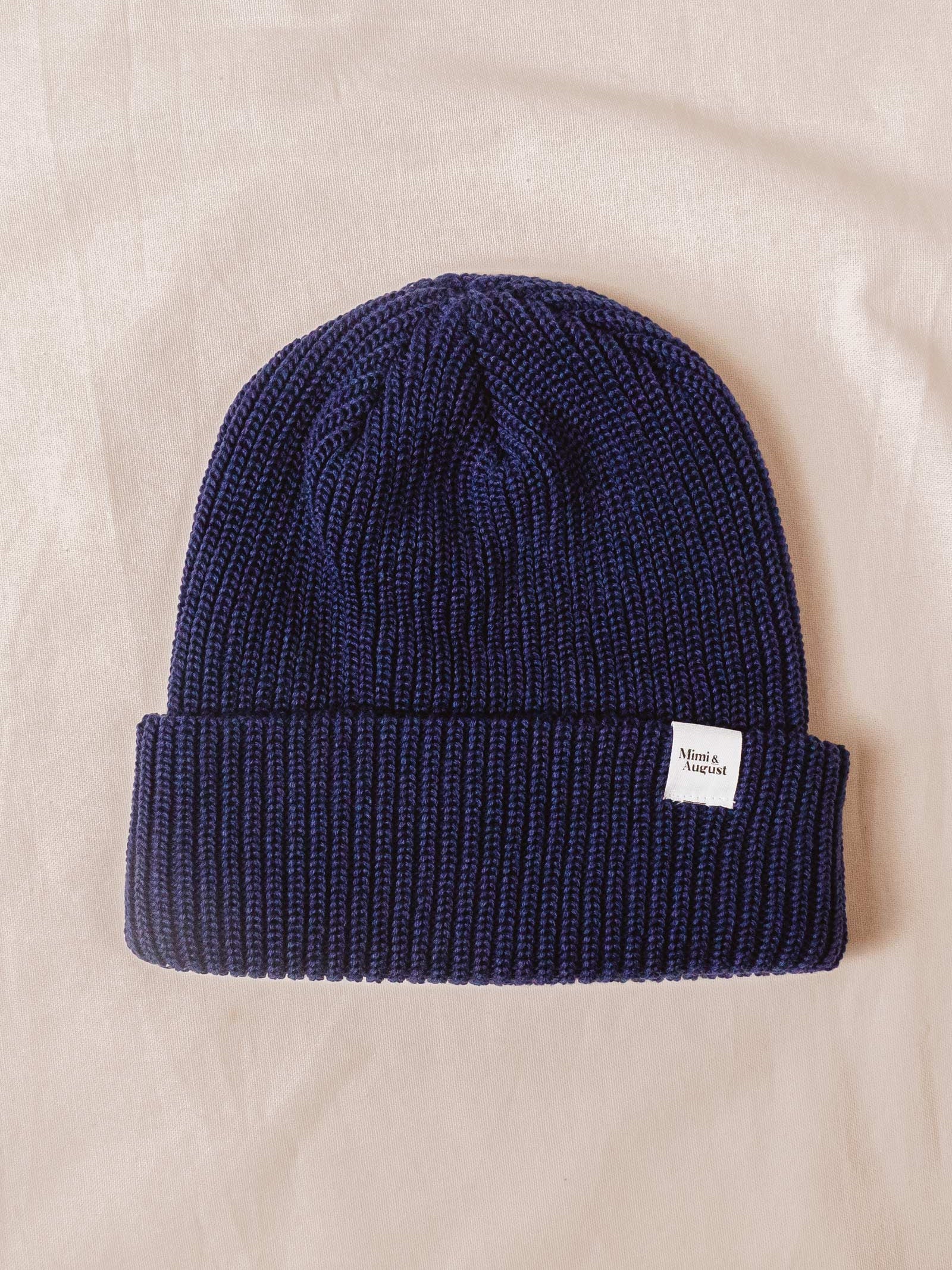 A Deep Blue Cuffed Beanie by mimi and august on a bed.
