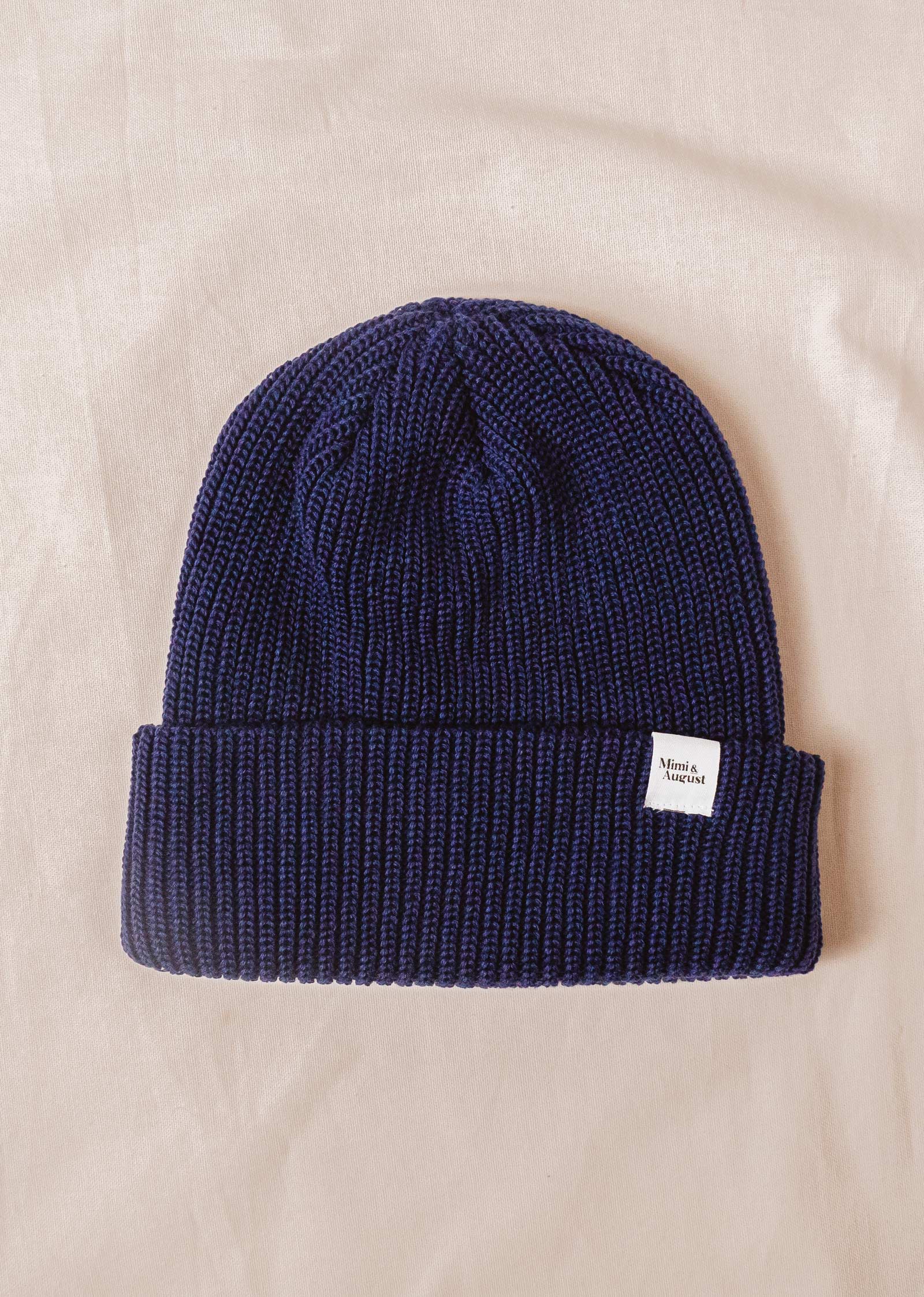 A Deep Blue Cuffed Beanie by mimi and august on a bed.