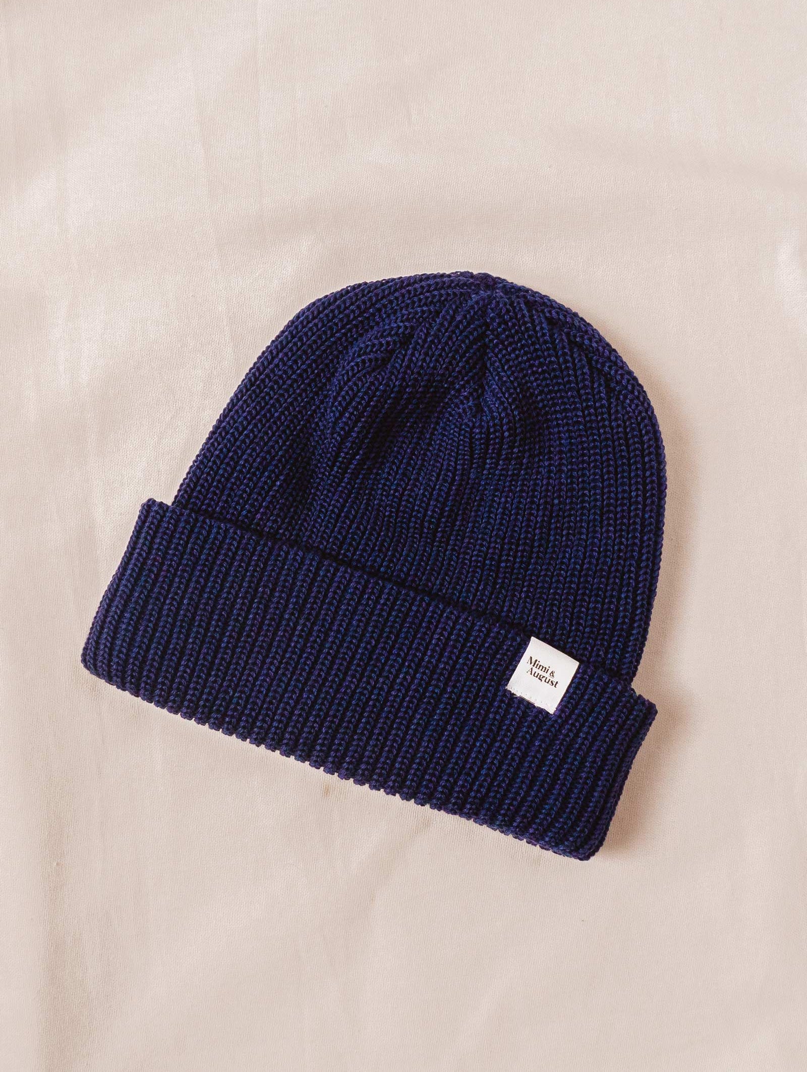 A Deep Blue Cuffed Beanie knit beanie on a bed.