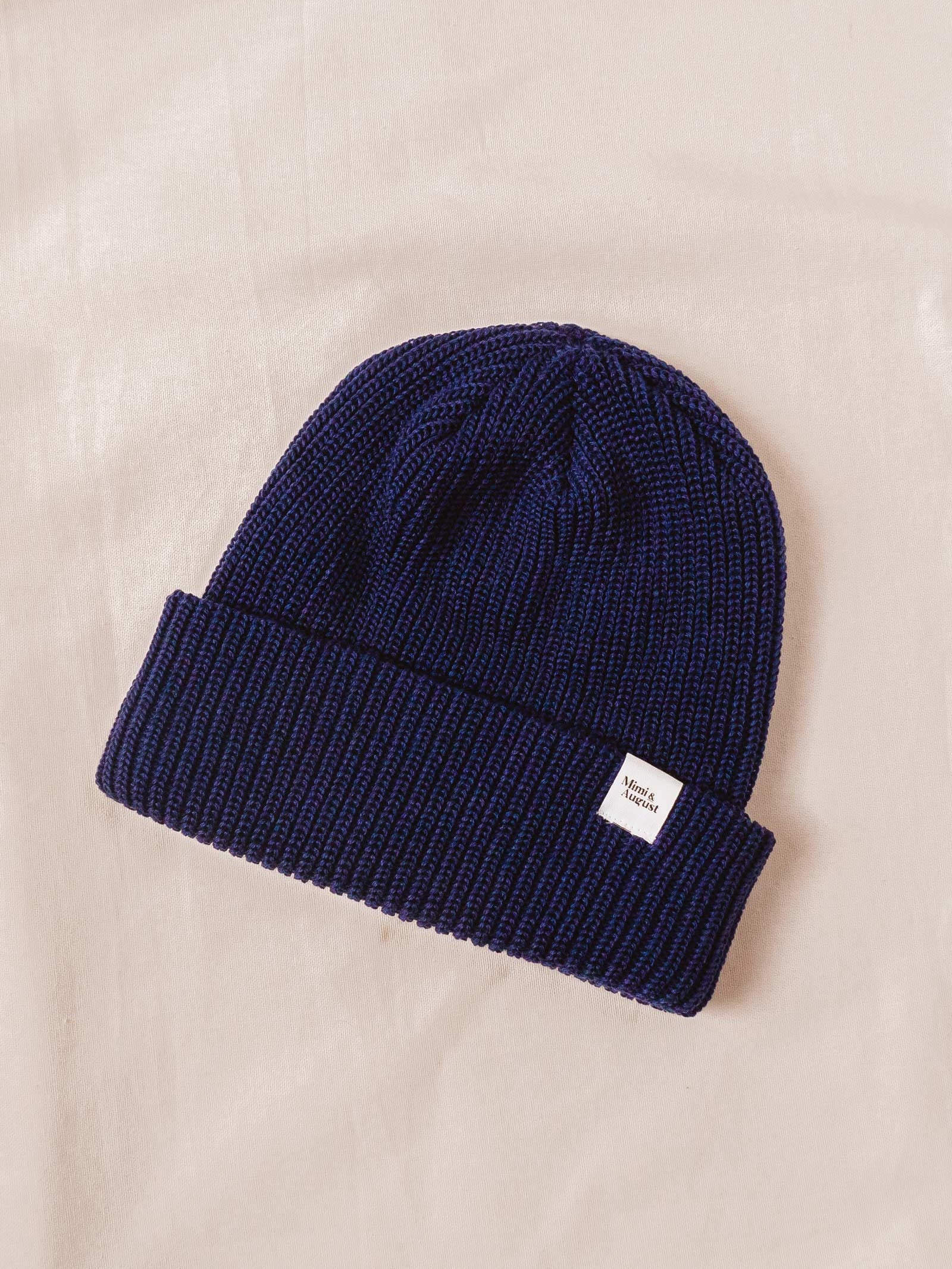 A Deep Blue Cuffed Beanie knit beanie on a bed.