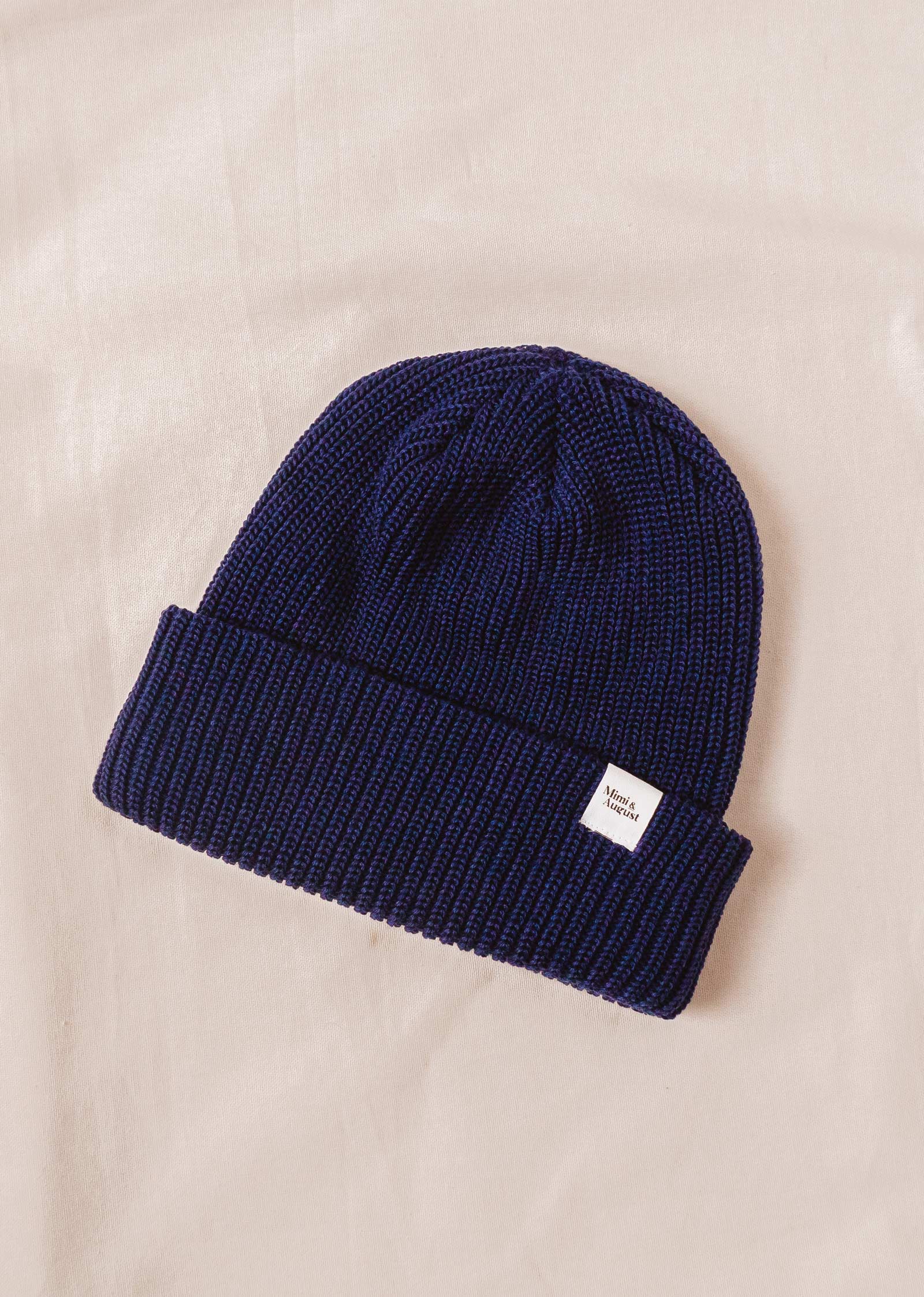 A Deep Blue Cuffed Beanie knit beanie on a bed.