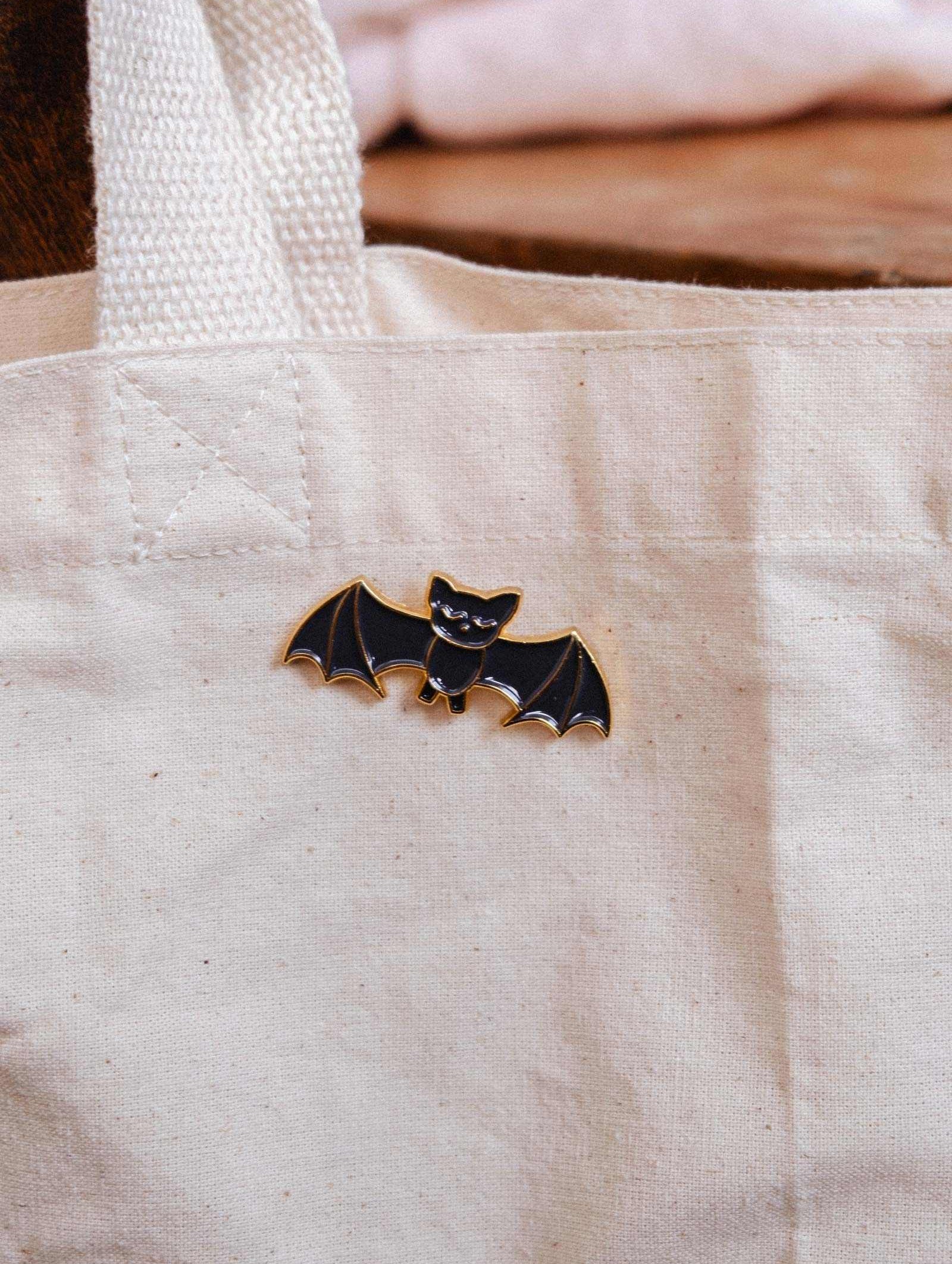 A canvas tote bag featuring the Mimi & August Little Bat Enamel Pin—a cute black bat accessory, perfect for animal lovers or adding charm to your style.