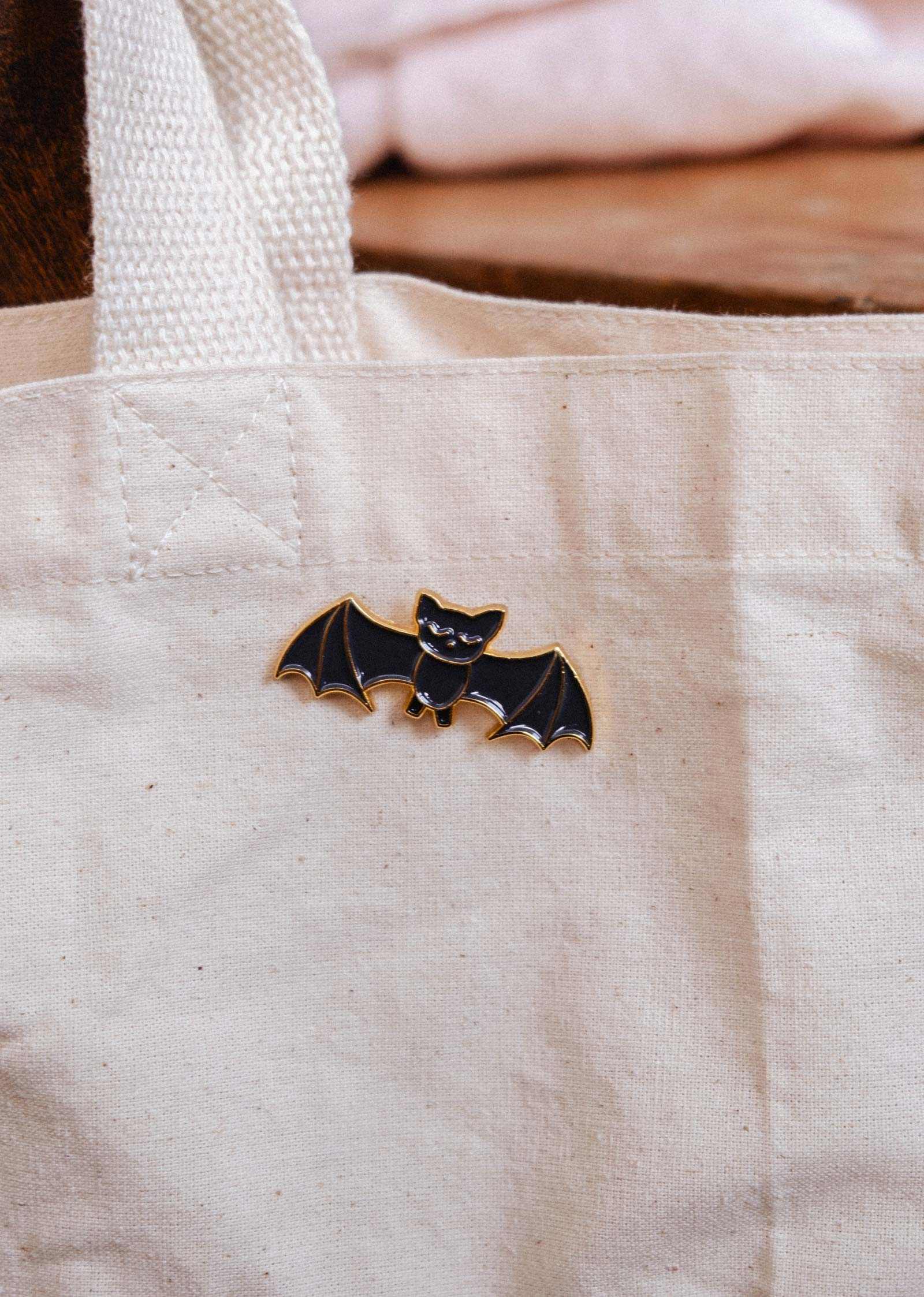 A canvas tote bag featuring the Mimi & August Little Bat Enamel Pin—a cute black bat accessory, perfect for animal lovers or adding charm to your style.
