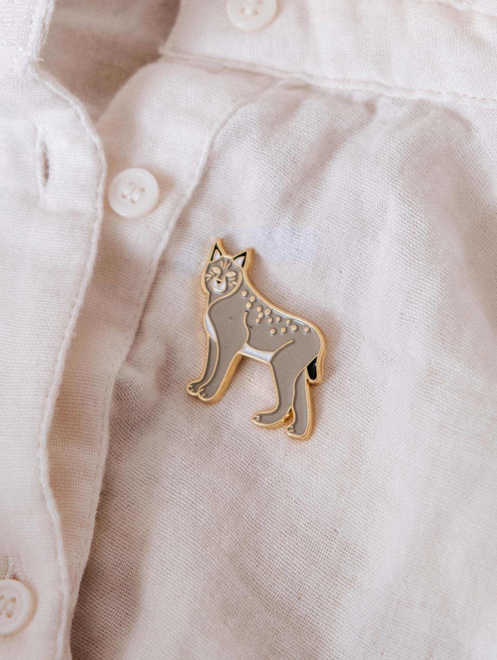 The Mimi & August Lynx Enamel Pin is displayed on a white button-up shirt, making it an ideal accessory for nature lovers and wildlife fans.