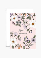 The Botanical Birthday Greeting Card by Mimi & August features "Joyeux anniversaire" on blush pink recycled paper, decorated with white and purple flowers plus green leaves. Includes a partially visible envelope.