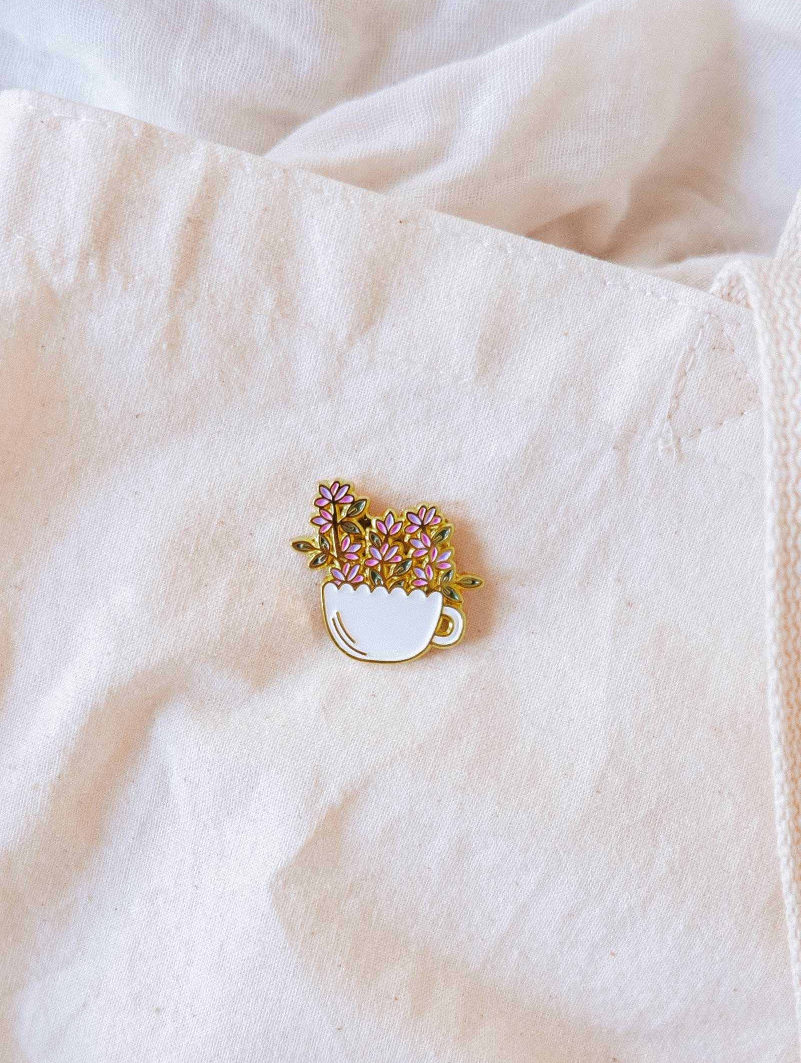 Bloom Cup Enamel Pin featuring a gold-tone teacup overflowing with flowers symbolizing joy and growth