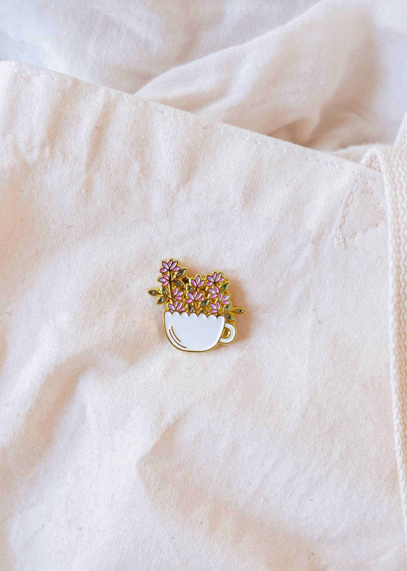Bloom Cup Enamel Pin featuring a gold-tone teacup overflowing with flowers symbolizing joy and growth