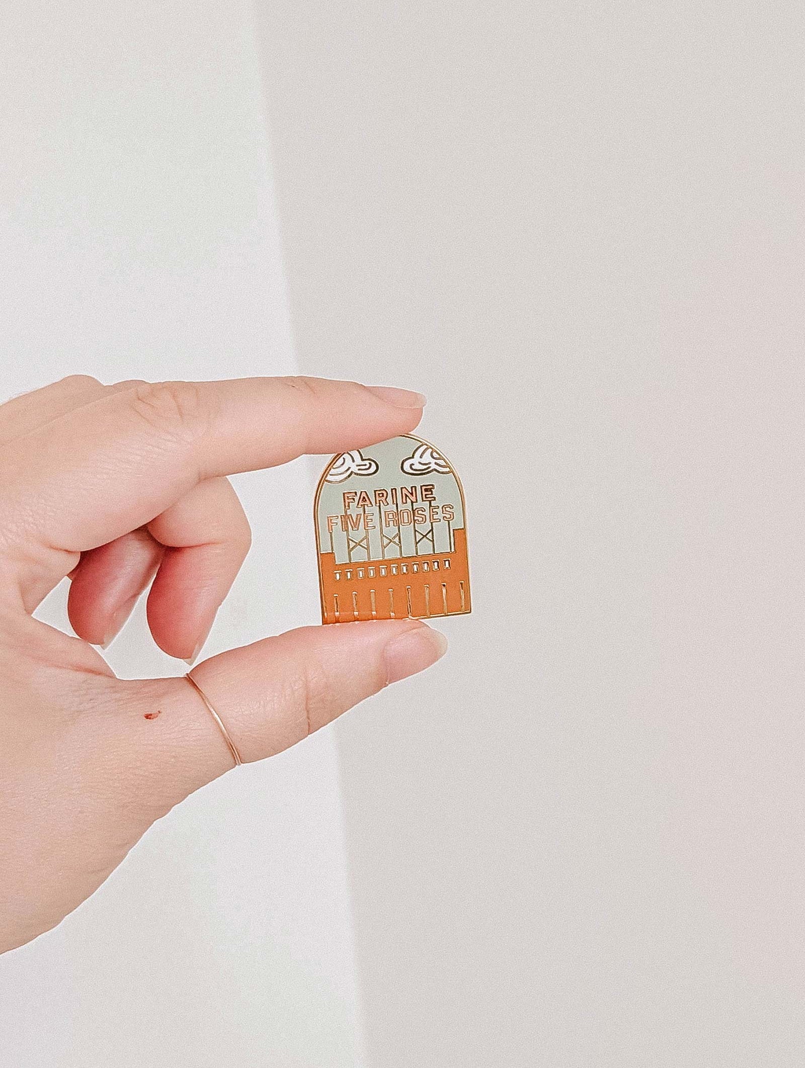 A hand holds the Mimi & August Flour & Roses Factory Enamel Pin, shaped like a brown comb with "Father, I've done my best" and a retro-inspired design.