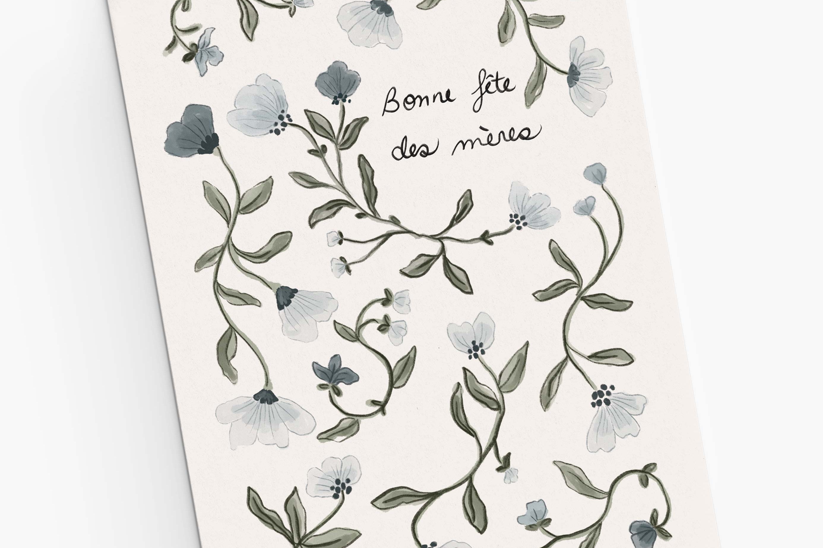 The Mimi & August Blue Flower Mother's Day Greeting Card features hand-drawn blue florals and green leaves framing the French text "Bonne fête des mères" on a white background, printed on recycled paper for an eco-friendly touch.