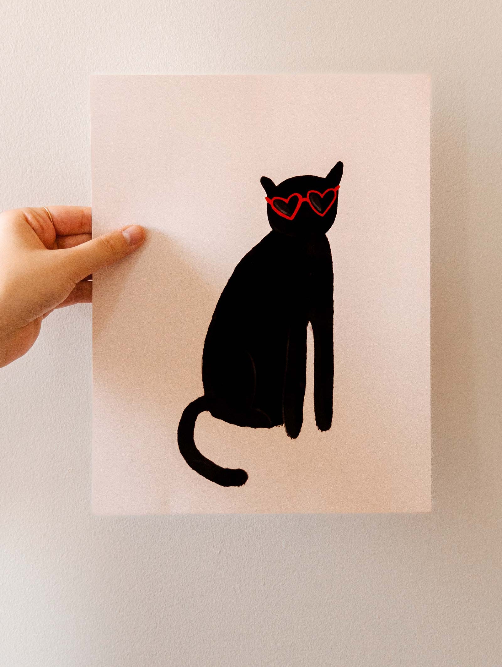 A quirky Mimi & August Heart Black Cat Art Print featuring a person holding a black cat with glasses.