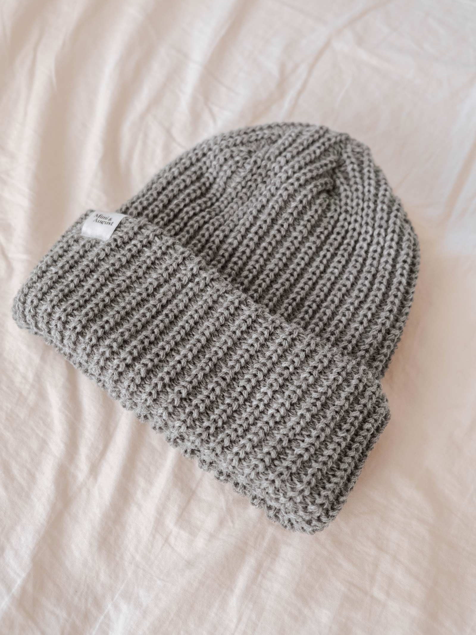 A Heather Grey Chunky Beanie from Mimi & August, crafted from chunky yarn with a folded brim, lies flat on a white surface. This cozy winter accessory is perfect for chilly days.