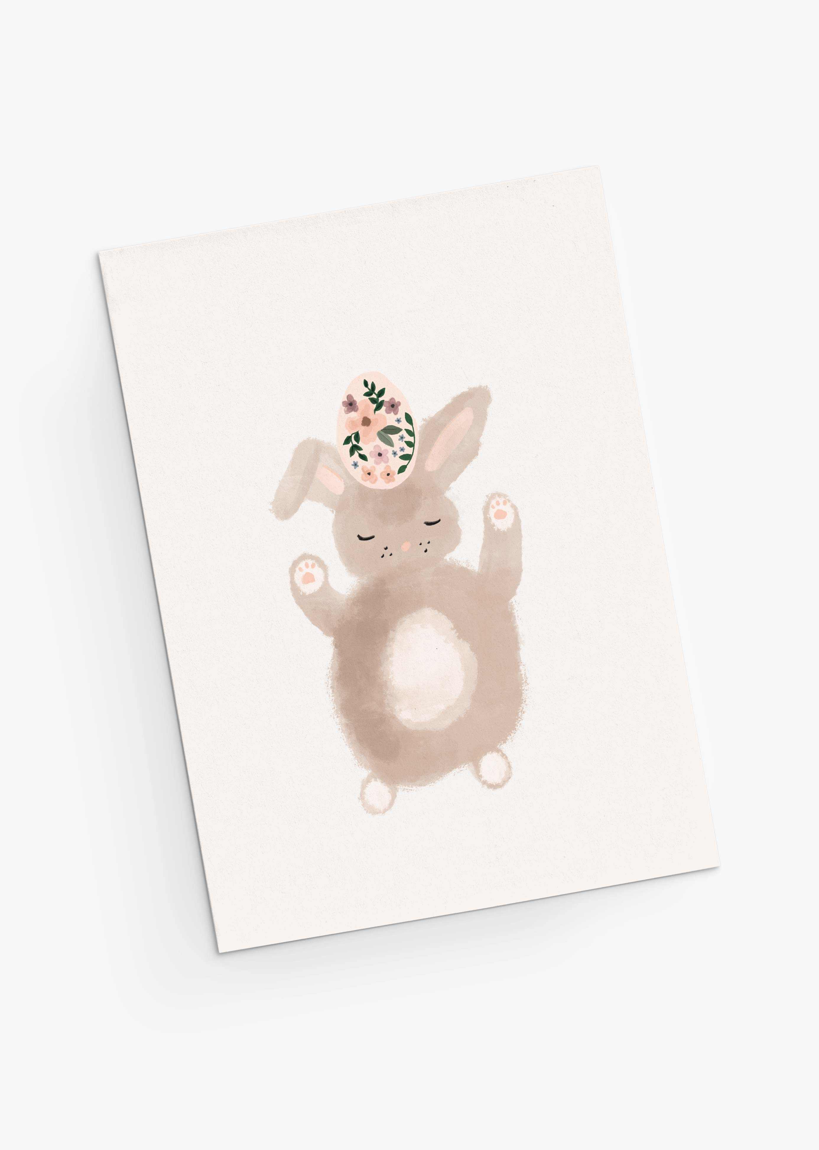 The Lapinot Greeting Card from Mimi & August features a cute bunny with closed eyes balancing a floral-patterned egg on its head. Rendered in delicate watercolor, it perfectly encapsulates springtime whimsy, making it ideal for an Easter card.