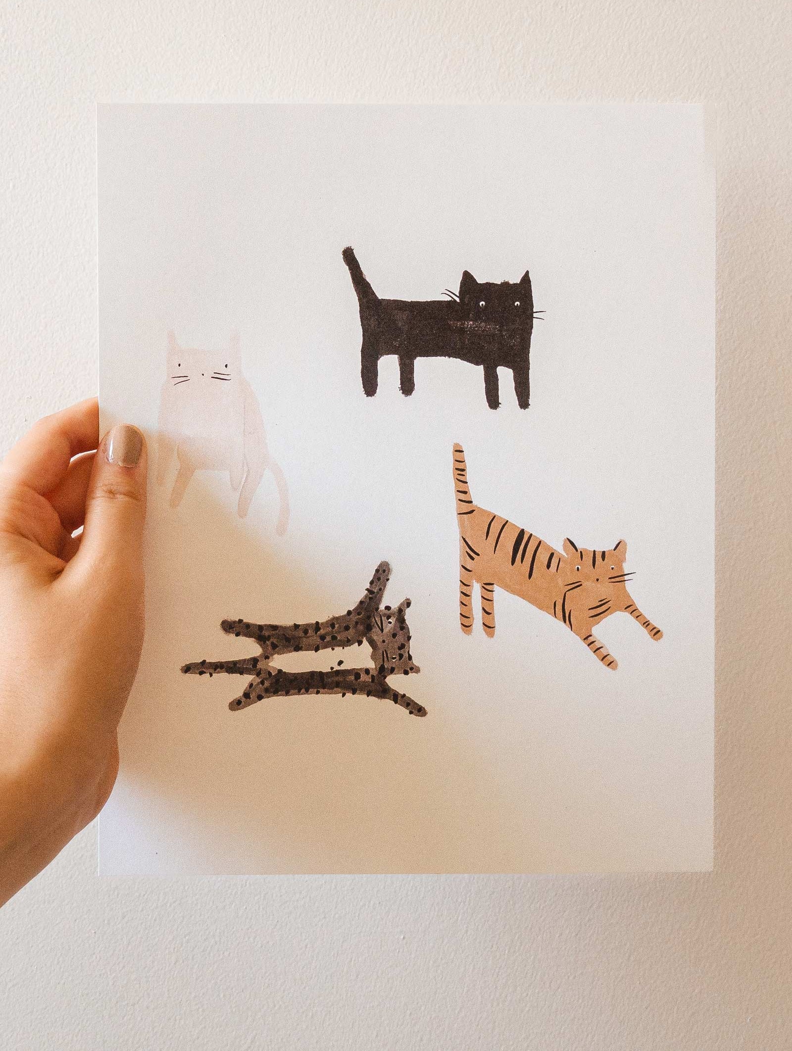 A person holding up an illustration with four cats on it by mimi and august