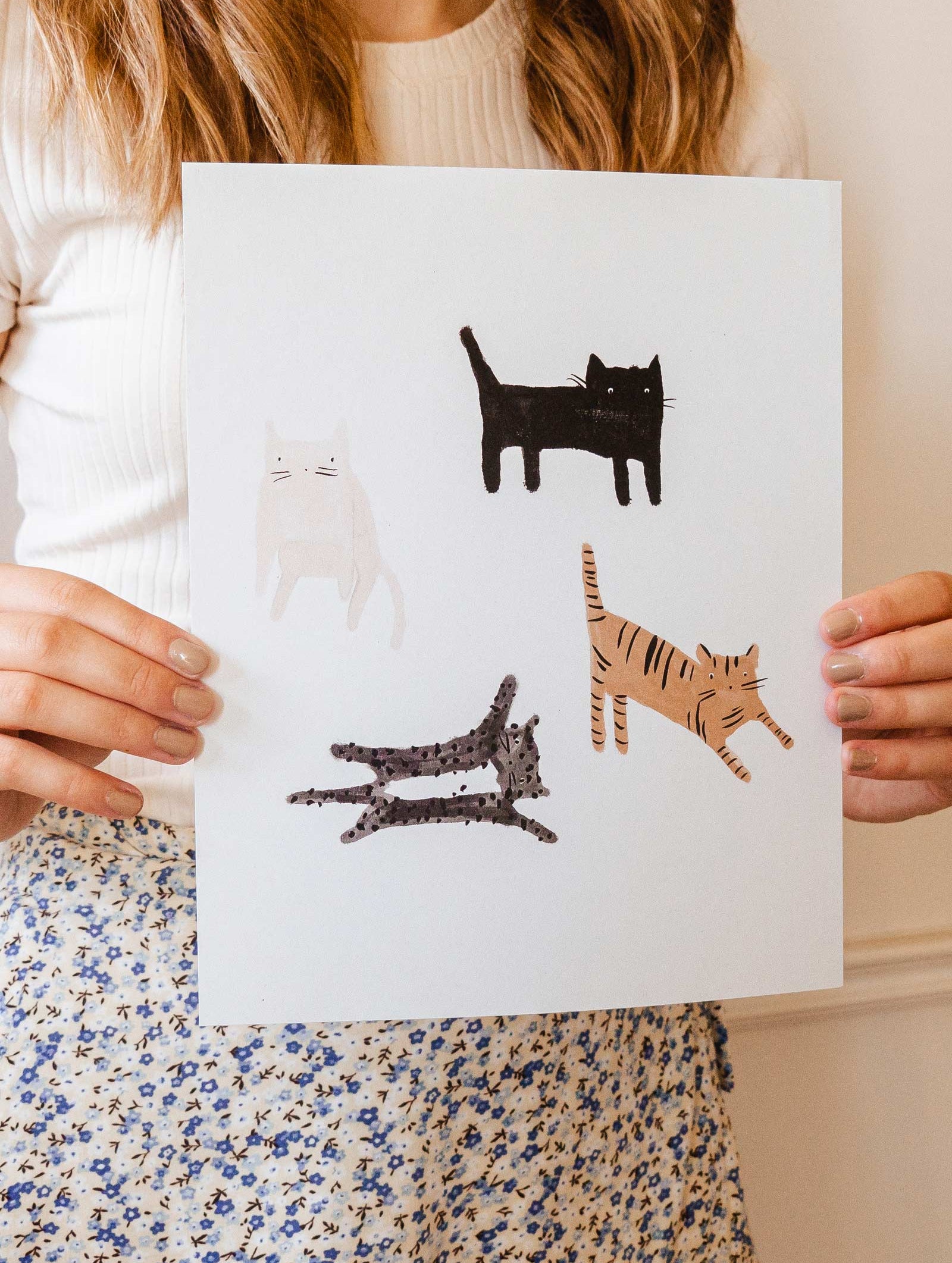 A girl holding up an illustration about four funny cats on it.