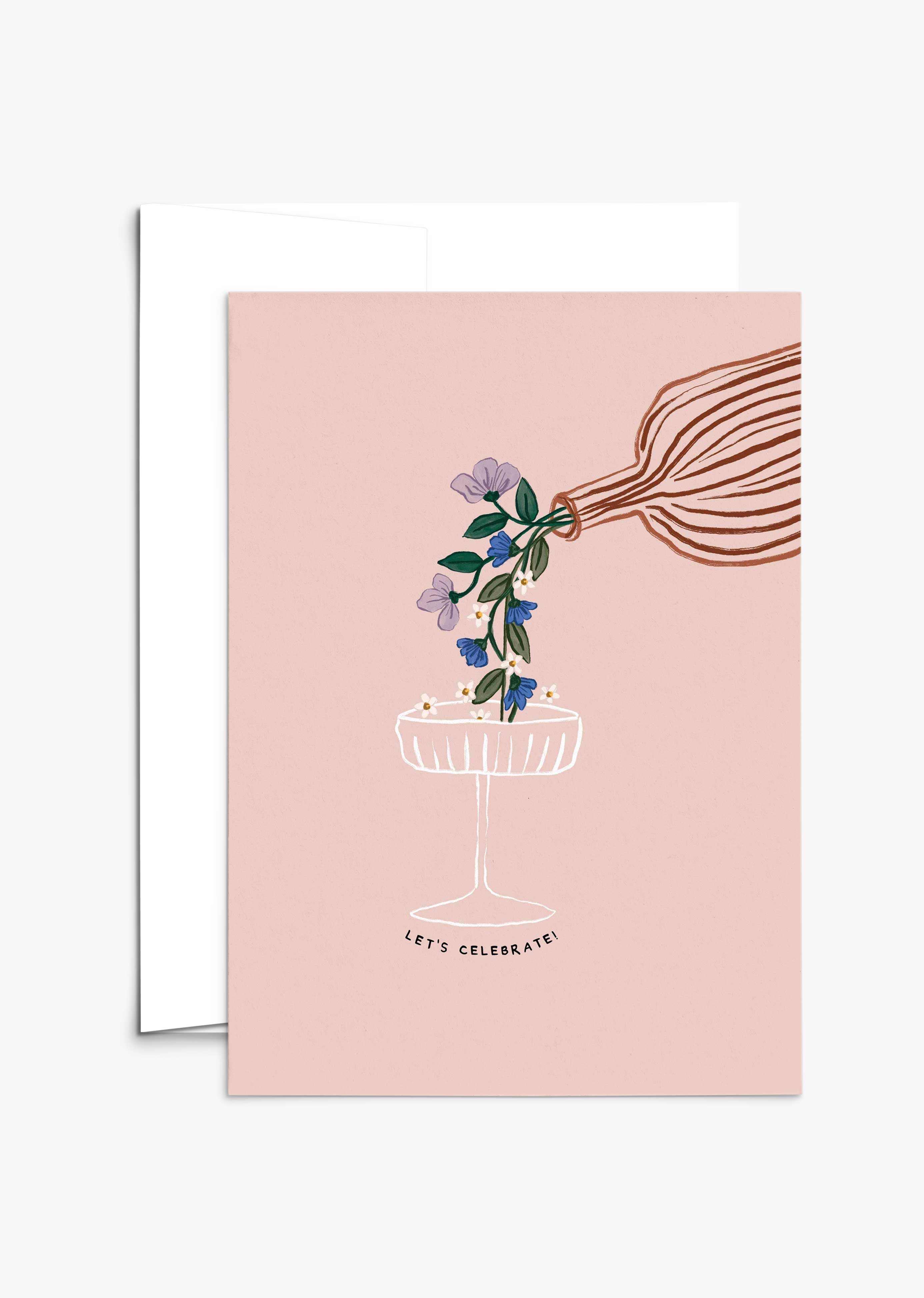 The Let's Celebrate Greeting Card by Mimi & August features a hand pouring flowers into a champagne glass on a pink background with "LET'S CELEBRATE!" below. Printed on recycled paper, it's the perfect card for any celebration.