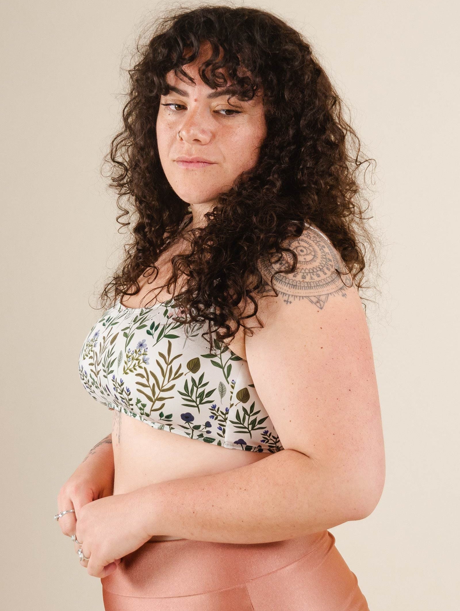 A woman wearing the mimi and august Floral Herboria Bralette Bikini Top and with a tattoo on her arm posing for a picture.