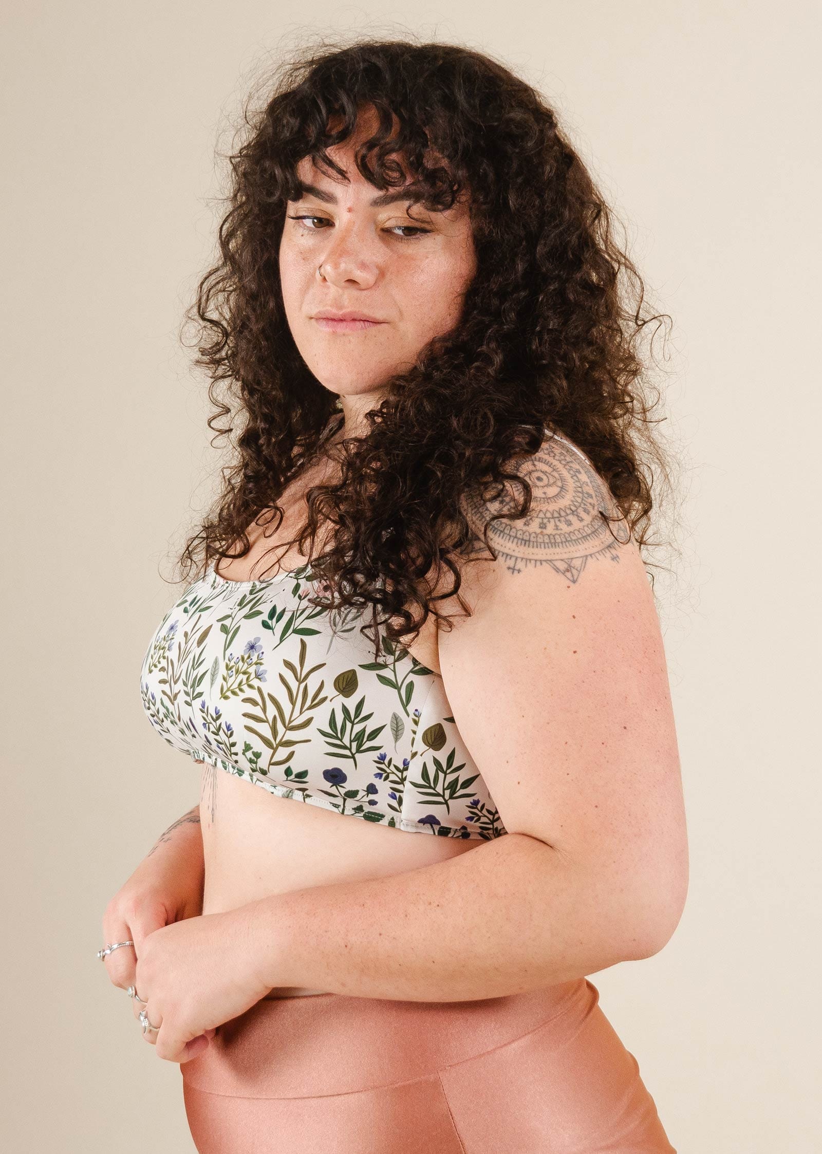 A woman wearing the mimi and august Floral Herboria Bralette Bikini Top and with a tattoo on her arm posing for a picture.