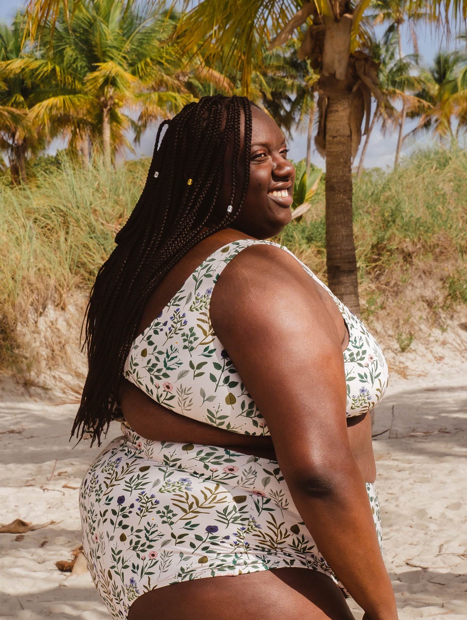 A woman in a mimi and august Lima Herboria Bralette Bikini Top, with white and green colors, standing on a beach.