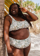African woman in a mimi and august Lima Herboria Bralette Bikini Top standing next to palms.