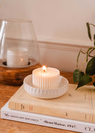 A lit Little Ceramic Nest by Mimi & August sits on a pile of books, one of which reads "My curves are not crazy. - Henri Matisse, 1947." A plant is visible in the background.