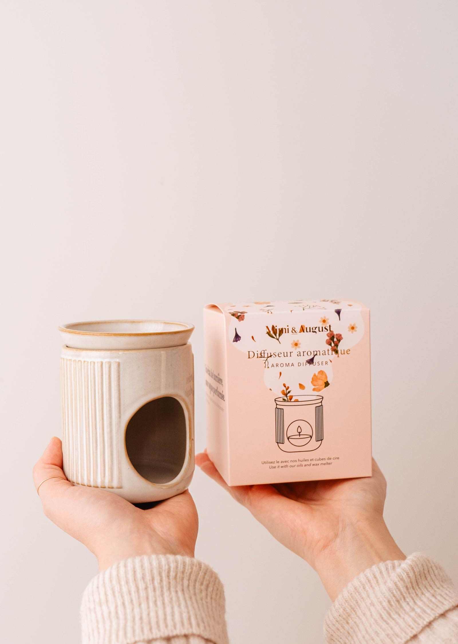 Hands holding the Lueur – Aromatic Ceramic Diffuser and a pink floral design box, ideal for pairing with scented oils from Mimi & August.