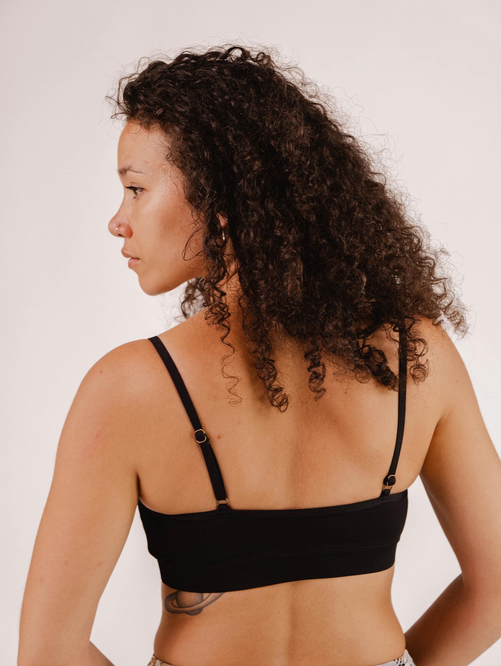Person with curly hair wearing a Mimi & August Mango Black Bralette Bikini Top with adjustable straps, viewed from the back and slightly to the side against a plain background.