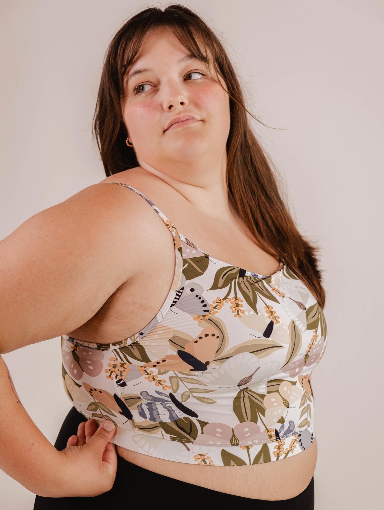A person in a Mango Mariposa Bralette Bikini Top by Mimi & August with adjustable straps looks to the side, standing against a plain background.